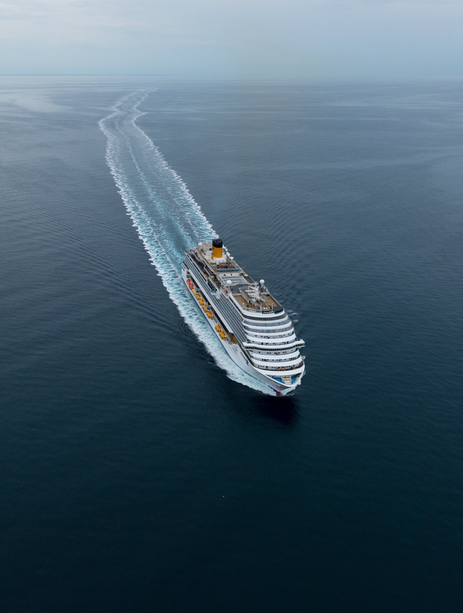 Fincantieri | Group - Business - Products - Cruise Ships - Costa Diadema: Large cruise ship in operation navigating calm open ocean waters, visible wake behind, overcast skies and expansive sea views, multiple decks and vibrant accents emphasize grandeur and scale.