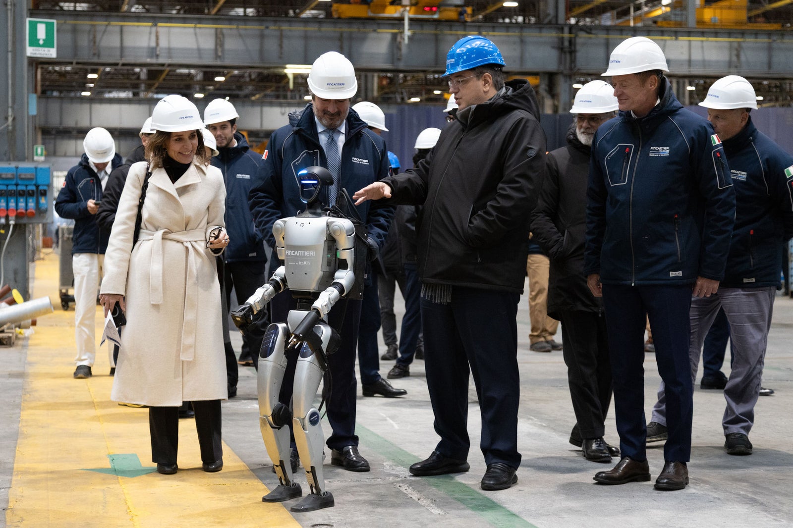  Newsroom - Comunicati stampa - 2025 - Gruppo Fincantieri: Fincantieri: visita del Commissario Europeo Apostolos Tzitzikostas al cantiere di Monfalcone: Il Commissario Europeo Apostolos Tzitzikostas e la delegazione Fincantieri osservano un robot avanzato all’interno del cantiere navale di Monfalcone, tutti con abbigliamento di sicurezza e caschi, ambiente industriale moderno.