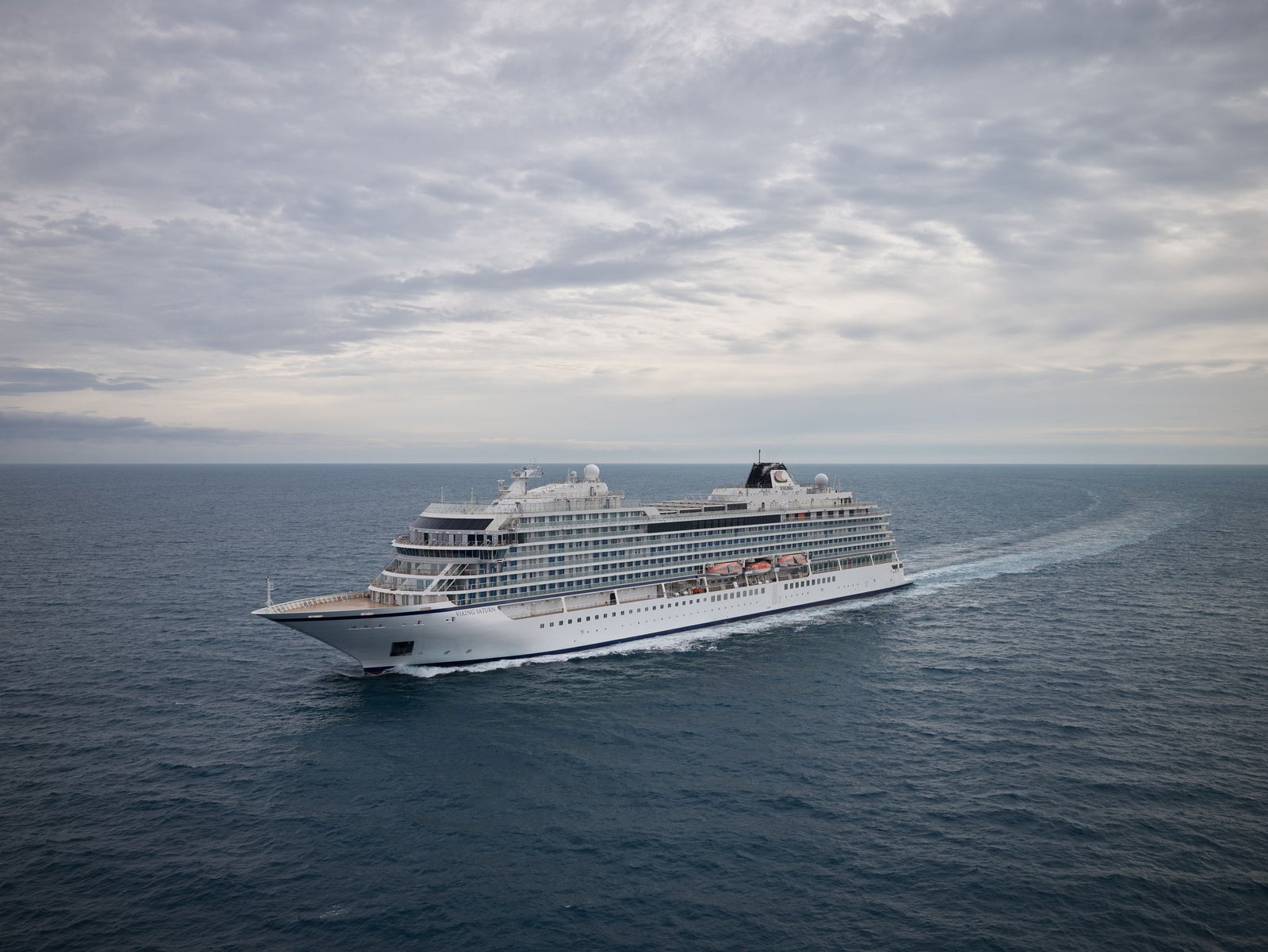  Fincantieri | Gruppo - Business - Prodotti - Navi da Crociera - Viking Saturn: Grande nave da crociera moderna operativa, naviga su acque oceaniche calme sotto cielo nuvoloso, molteplici ponti e architettura elegante, nessuna terra visibile, scenario di tranquillità e vastità marina.