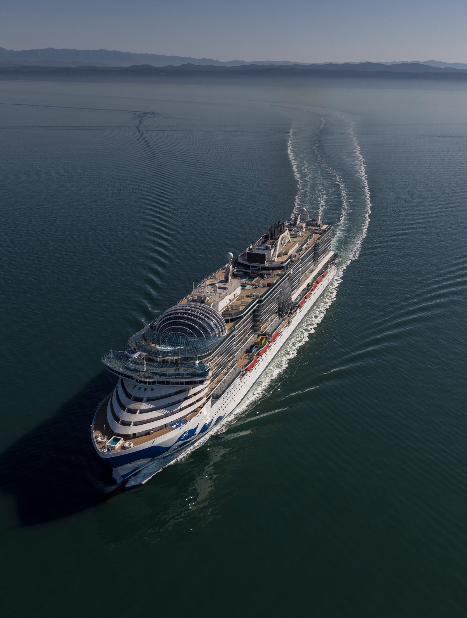  Fincantieri | Gruppo - Business - Prodotti - Navi da Crociera - Star Princess: Massive cruise ship in operation, navigating calm open waters, multiple decks, sleek design, visible wake, distant mountains on horizon, clear sky.