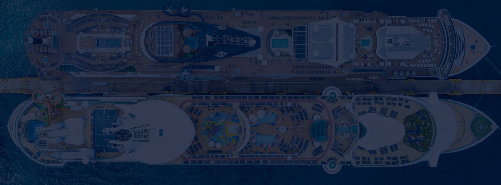 Fincantieri | Group - Sustainability - Industrial Excellence - Products: Top-down view of two large cruise ships docked side by side in port, spacious decks with pools, relaxation areas, and recreational spaces; deep blue water surrounding them, detailed layout showcasing luxury amenities and design.
