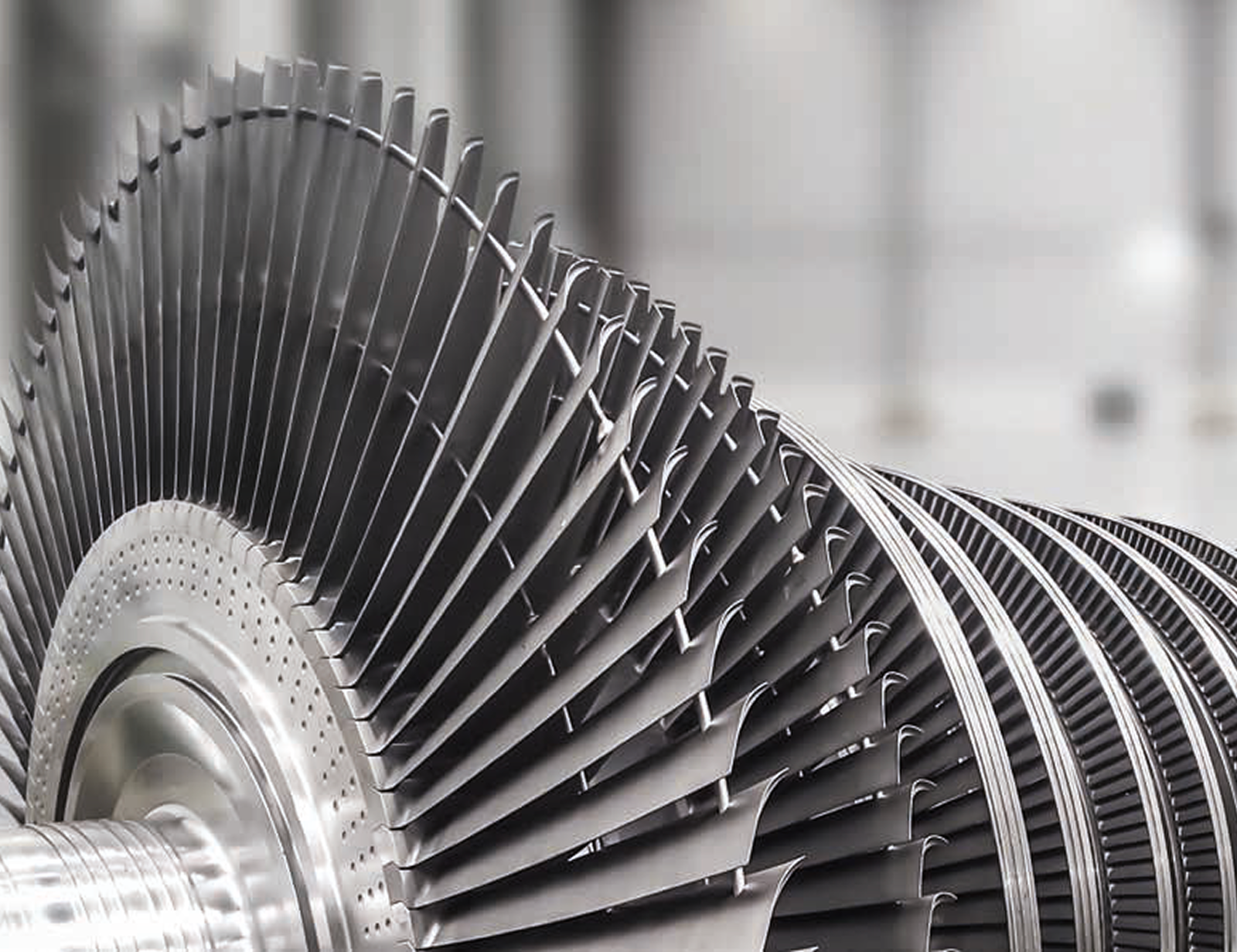  Fincantieri | Group - Business - Products - Equipment, Systems and Infrastructures - Steam turbines: Close-up of turbine rotor with numerous curved blades, metallic component viewed from the side, showing intricate design.