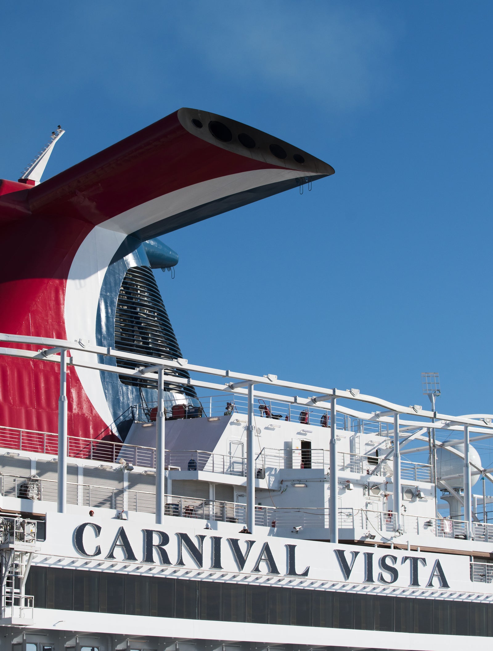 Fincantieri | Group - Business - Products - Cruise Ships - Carnival Vista: Aerial view of Carnival Vista cruise ship docked under clear blue sky, prominent red and white funnel, Carnival Vista name clearly readable on side, upper deck with recreation areas and structural details, static vessel.