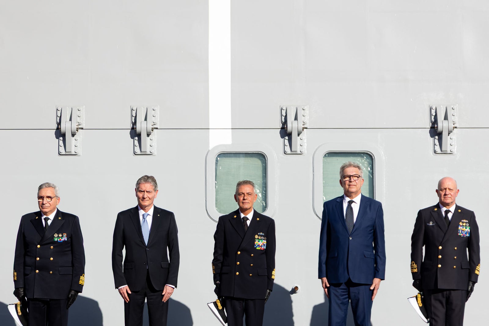 newsroom - press releases - 2025 - fincantieri group: fincantieri delivers "atlante", second lss unit for the italian navy: five officers and representatives in uniform and suit standing in line against the hull of the "atlante", portholes and sunlight.