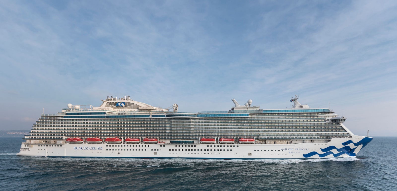 Fincantieri | Group - Business - Products - Cruise Ships - Majestic Princess: Large operational luxury cruise ship sailing on calm ocean waters under partly cloudy sky, blue wave design on hull, multiple decks with visible balconies, setting evokes travel and leisure, ideal for vacation or maritime exploration.