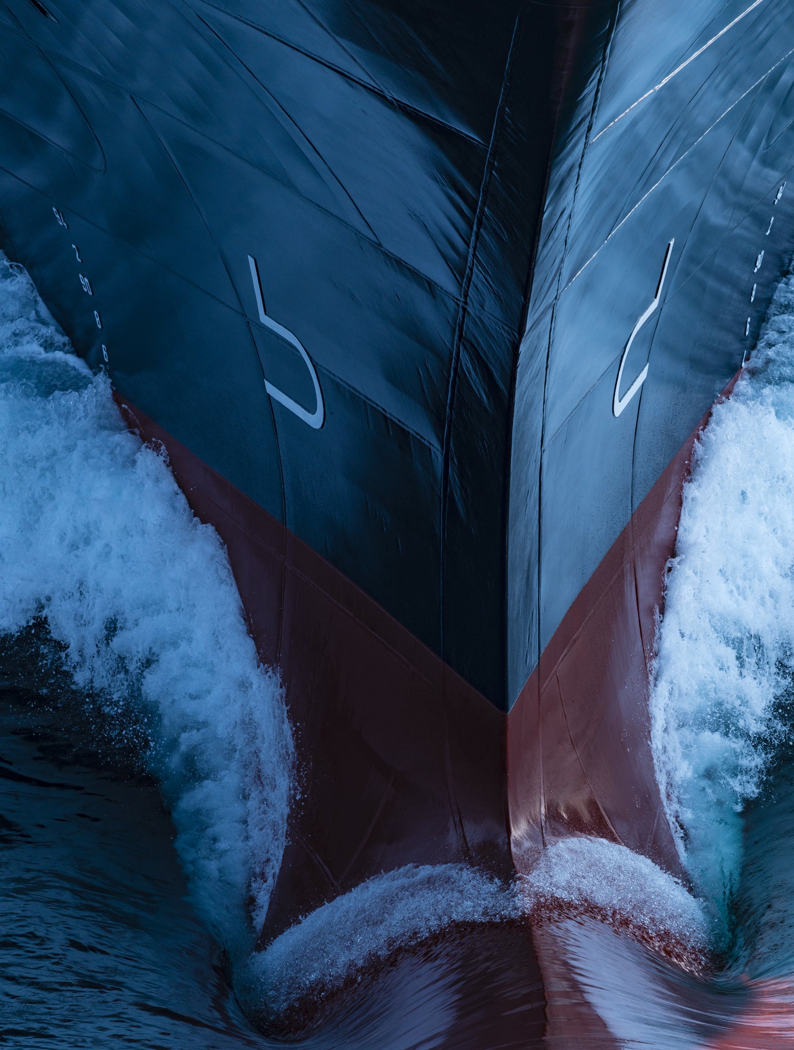 Fincantieri | Gruppo - Business - Prodotti - Navi da Crociera - Nieuw Statendam: Primo piano della prua della Nieuw Statendam operativa che taglia l’oceano, onde dinamiche e schizzi, design elegante con marcature visibili sullo scafo, illuminazione che evidenzia contrasto tra acque blu profonde e toni rossastri della parte inferiore, enfatizza movimento e potenza.