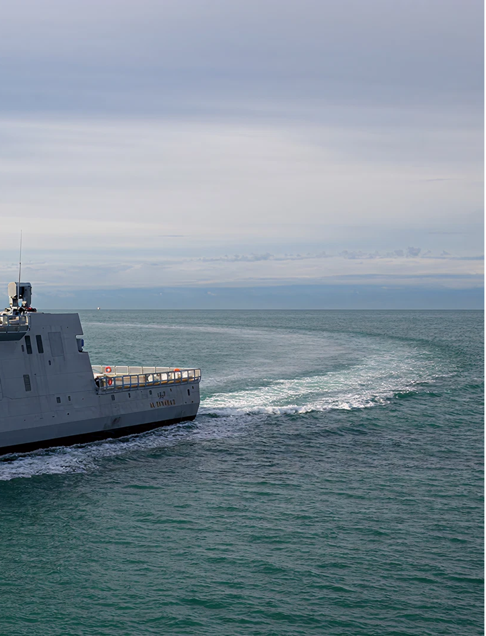 Fincantieri | Gruppo - Società - Controllate e collegate - Fincantieri Services Doha: Grande nave navale ‘L 17 HDMS’ operativa in navigazione su acque calme sotto cielo nuvoloso, scia visibile, design industriale della nave in contesto marino tranquillo.