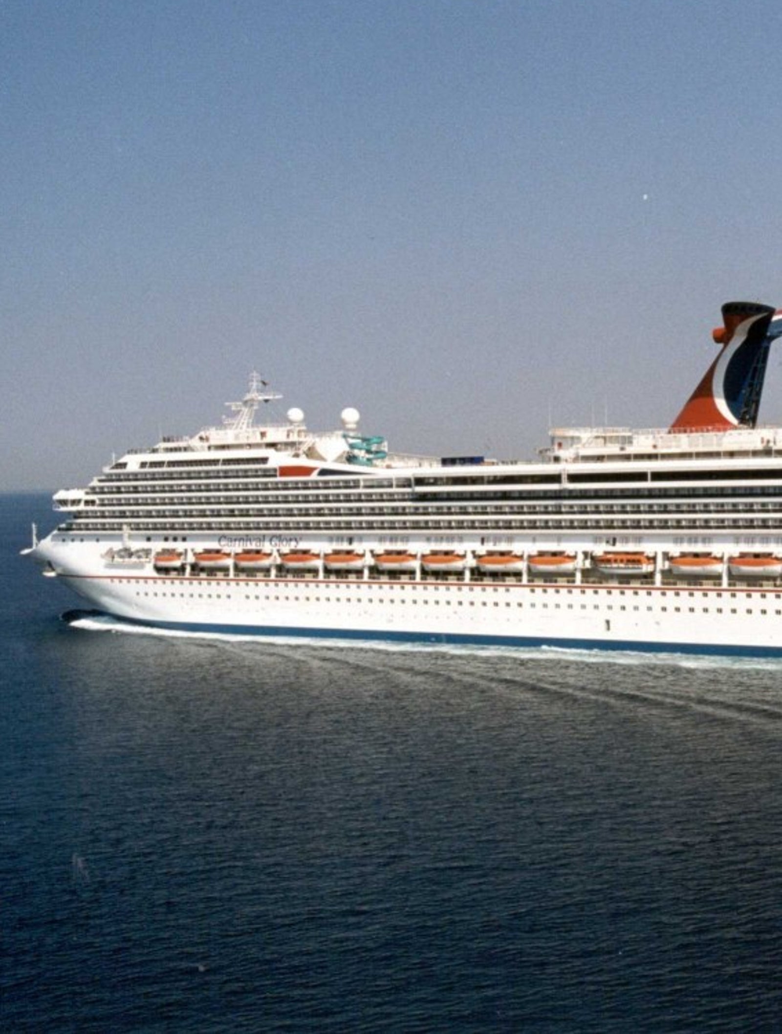 Fincantieri | Group - Business - Products - Cruise Ships - Carnival Glory: Side view of Carnival Glory cruise ship in operation navigating, white hull, distinctive red and blue funnel, multiple passenger decks and visible lifeboats.