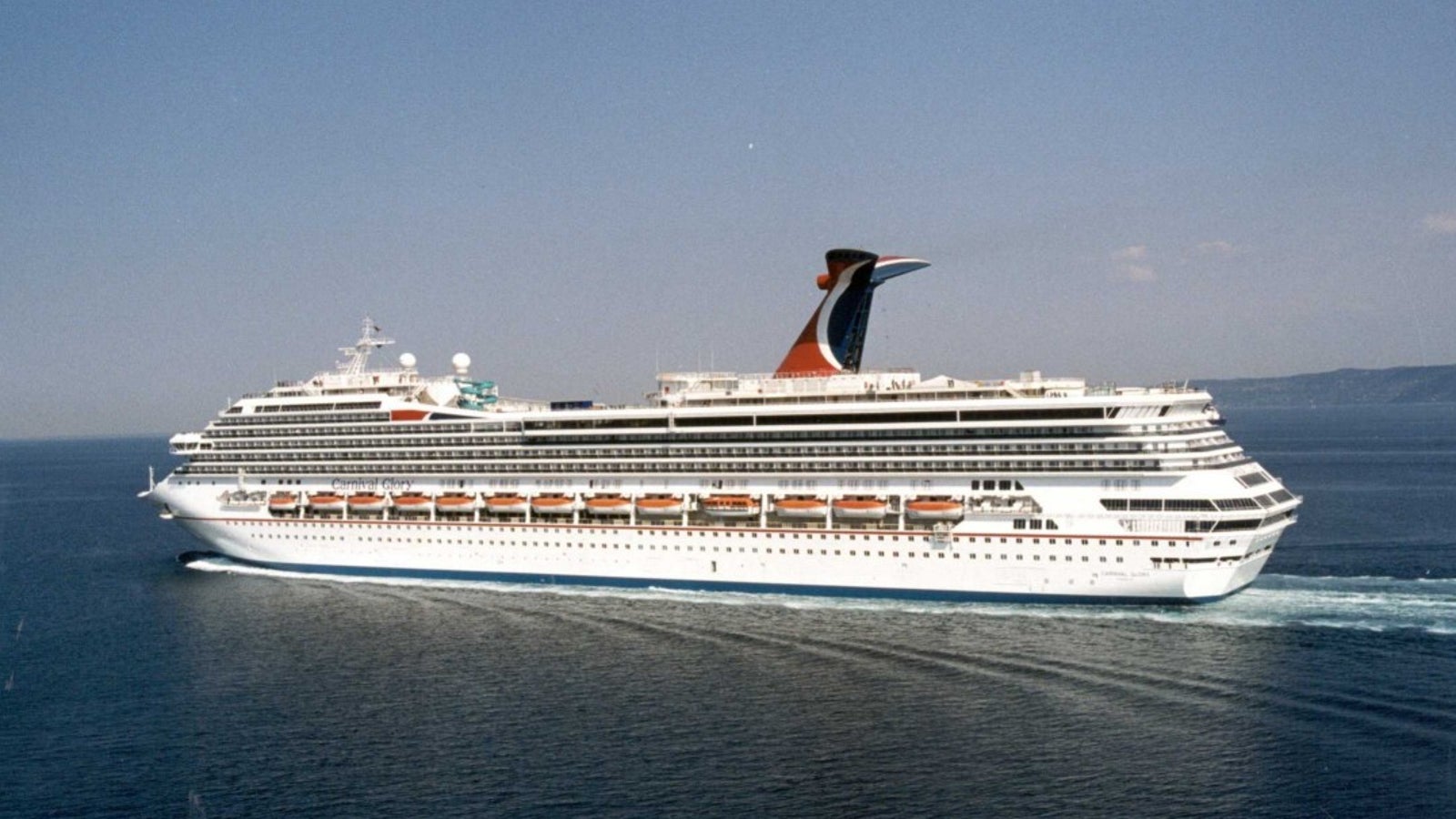 Fincantieri | Group - Business - Products - Cruise Ships - Carnival Glory: Side view of Carnival Glory cruise ship in operation, white hull, distinctive red and blue funnel, multiple passenger decks and visible lifeboats.