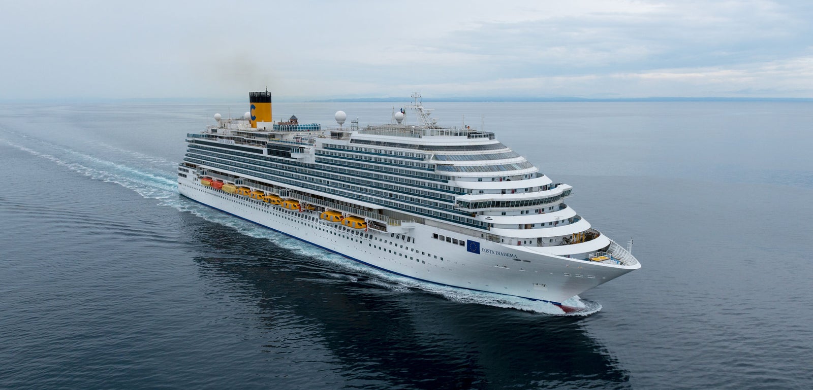 Fincantieri | Group - Business - Products - Cruise Ships - Costa Diadema: Massive cruise ship in operation gliding through calm open waters under cloudy sky, multiple decks, lifeboats, distinctive yellow funnel with visible markings, serene ocean setting highlights grandeur and scale, ideal for leisure travel and exploration.
