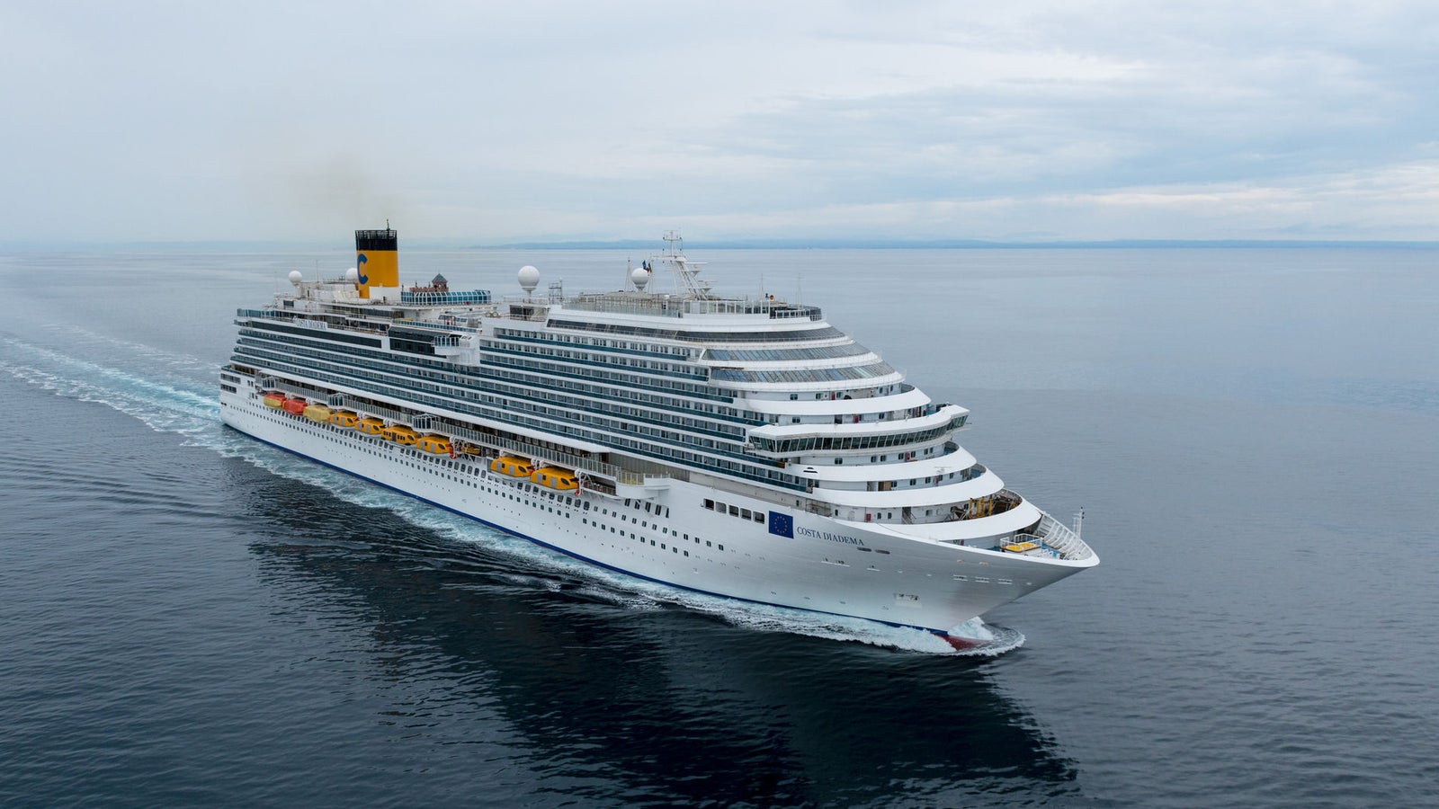Fincantieri | Group - Business - Products - Cruise Ships - Costa Diadema: Side view of Costa Diadema cruise ship in operation, hull with multiple passenger decks, visible lifeboats and yellow funnel with Costa markings.