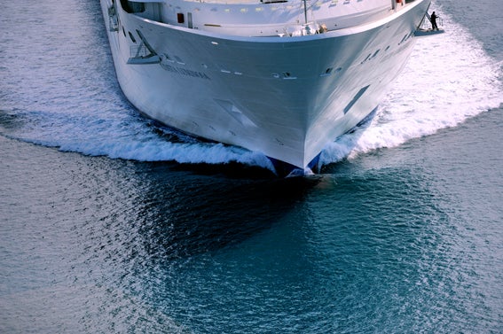 Fincantieri | Gruppo - Business - Prodotti - Navi da Crociera - Costa Luminosa: Grande nave da crociera operativa che scivola su acque blu calme, scia dinamica a prua, design filante ed esterno bianco ben visibili, viaggio marittimo sereno senza passeggeri o equipaggio visibili sul ponte.