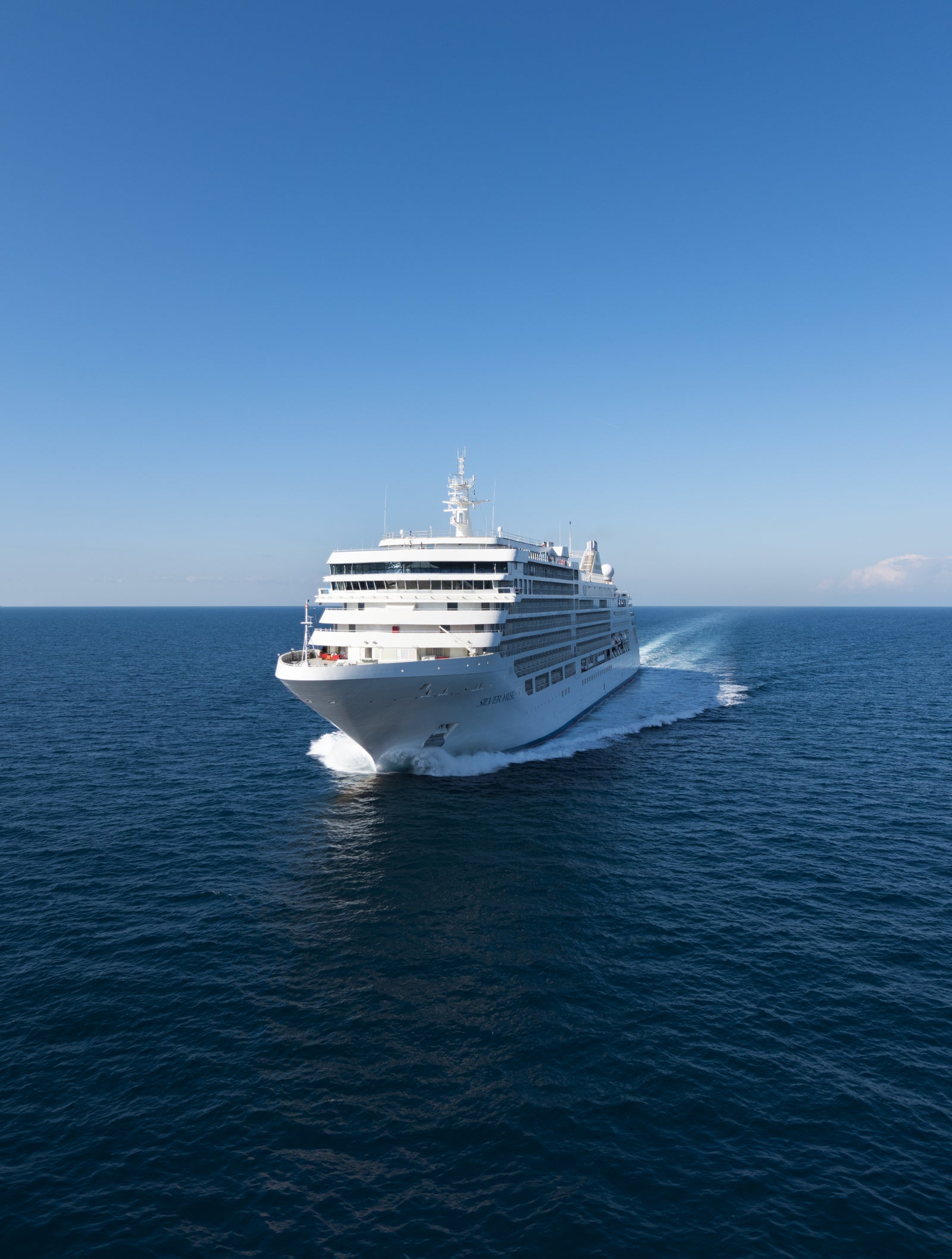 Fincantieri | Group - Business - Products - Cruise Ships - Silver Spirit: Large modern luxury cruise ship in operation, white with multiple decks and visible lifeboats, sailing on calm waters under partly cloudy sky, visible wake, scene highlights grandeur and elegance suitable for relaxing and sophisticated travel experiences.