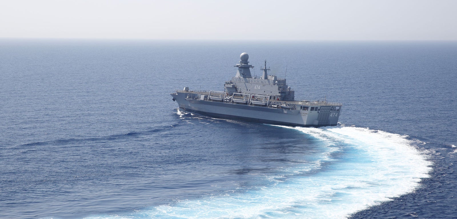 Prodotto - Nave Militare Kalat Beni-Abbes: Vista aerea della nave operativa in navigazione, virata con scia evidente, dotata di sistemi radar avanzati e attrezzature navali.