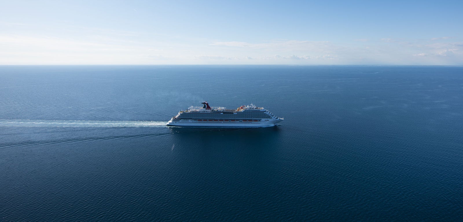 Fincantieri | Group - Business - Products - Cruise Ships - Carnival Vista: Large operational white cruise ship gliding on calm open waters under clear blue sky, light smoke emitted from funnel, visible wake in water, serene ocean setting emphasizes peaceful journey.