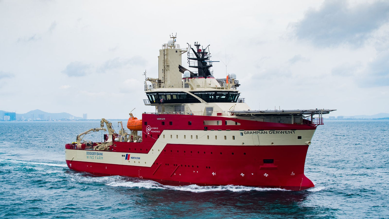 Prodotto - Offshore Support Vessel Derwent: Vista laterale della nave operativa in navigazione, scafo rosso, equipaggiamenti industriali visibili, nome Skandi Singapore sullo scafo, sfondo urbano costiero.