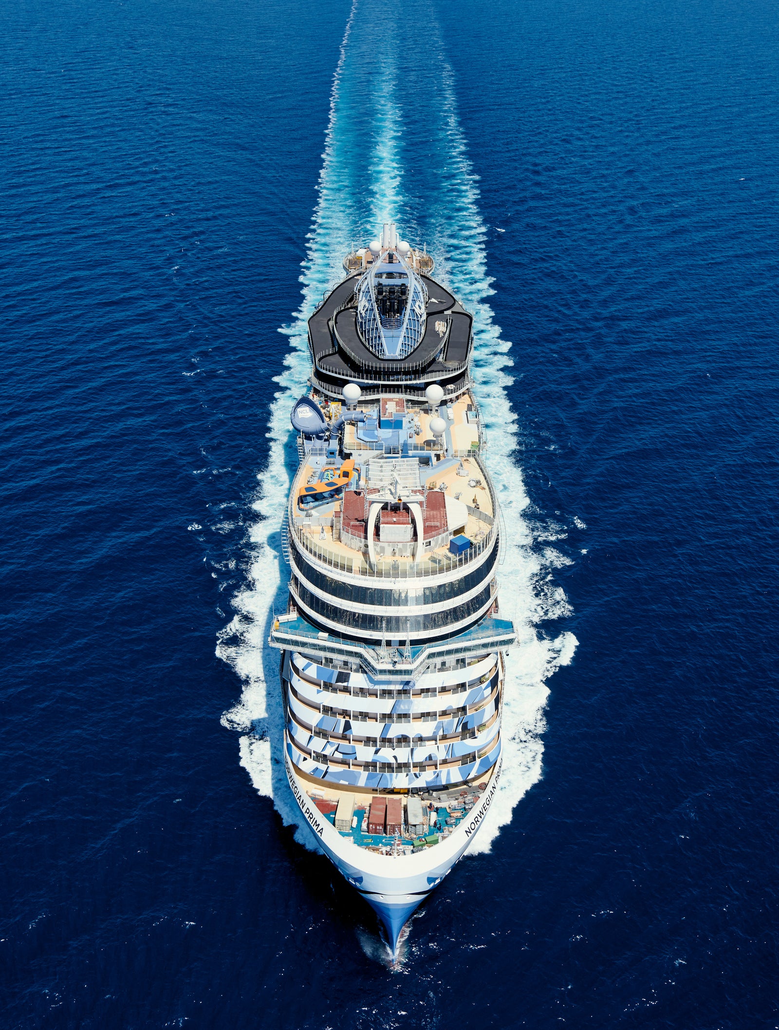 Fincantieri | Group - Business - Products - Cruise Ships - Norwegian Prima: Rear view of Norwegian Prima cruise ship in operation, multiple decks with outdoor areas, pools and seating, visible wake, modern leisure-oriented design.