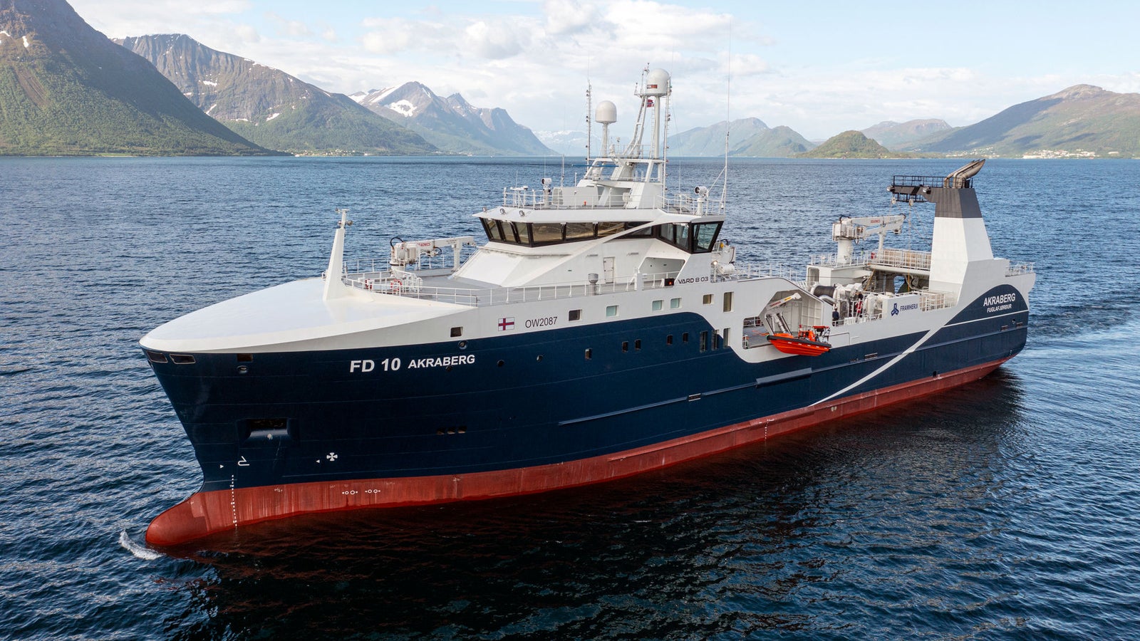 Prodotto - Peschereccio FD 10 Akraberg: Vista laterale della nave operativa in navigazione, scafo con nome FD 10 Akaberø ben visibile, design moderno, ambiente marittimo sereno con montagne sullo sfondo e cielo parzialmente nuvoloso.