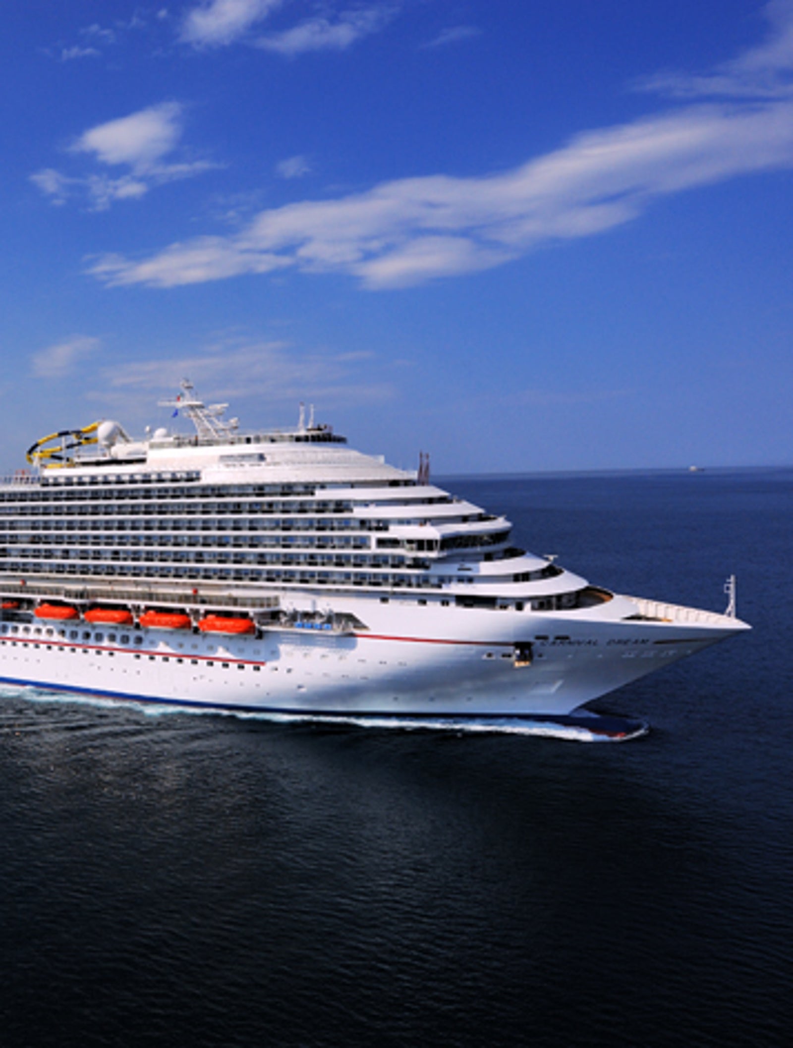 Fincantieri | Group - Business - Products - Cruise Ships - Carnival Dream: Massive cruise ship in operation gliding through calm open waters under bright blue sky, multiple decks, lifeboats, distinctive red funnel, serene ocean setting highlights grandeur and scale, ideal for leisure travel and exploration.