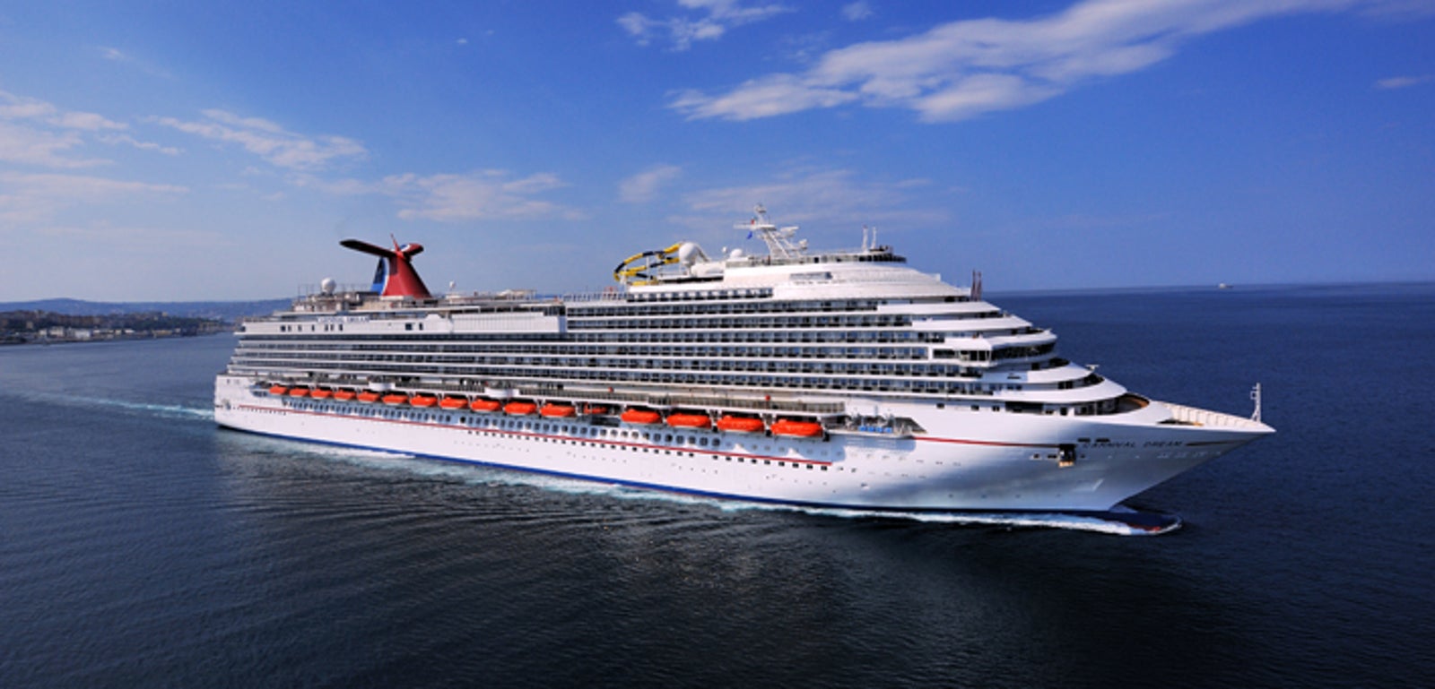 Fincantieri | Group - Business - Products - Cruise Ships - Carnival Dream: Massive cruise ship in operation gliding through calm open waters under bright blue sky, multiple decks, lifeboats, distinctive red funnel, serene ocean setting highlights grandeur and scale, ideal for leisure travel and exploration.