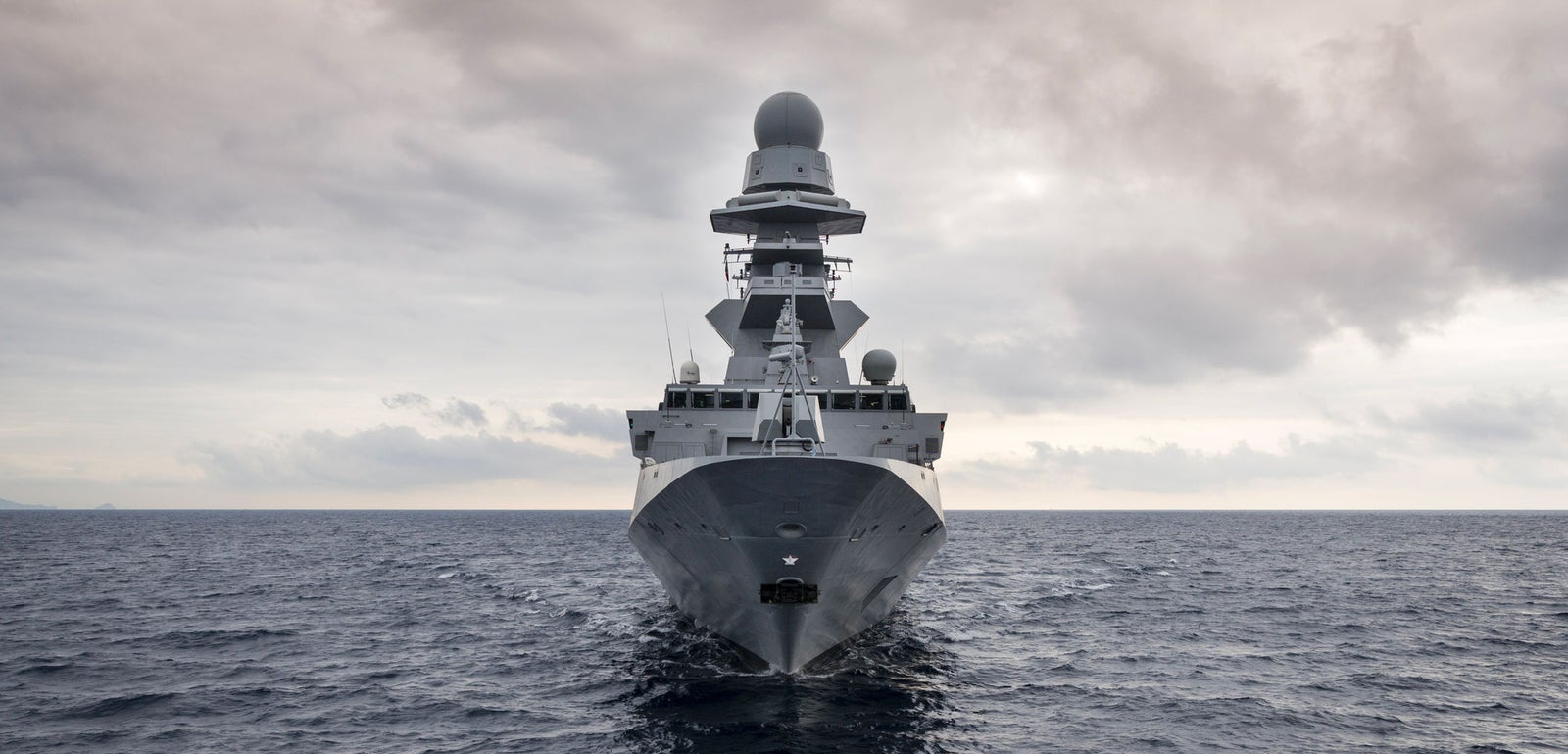 Fincantieri | Gruppo - Business - Prodotti - Navi per la difesa - Fregate - Classe Bergamini: Nave da guerra moderna vista frontalmente, in navigazione su mare mosso e grigio, cielo nuvoloso.