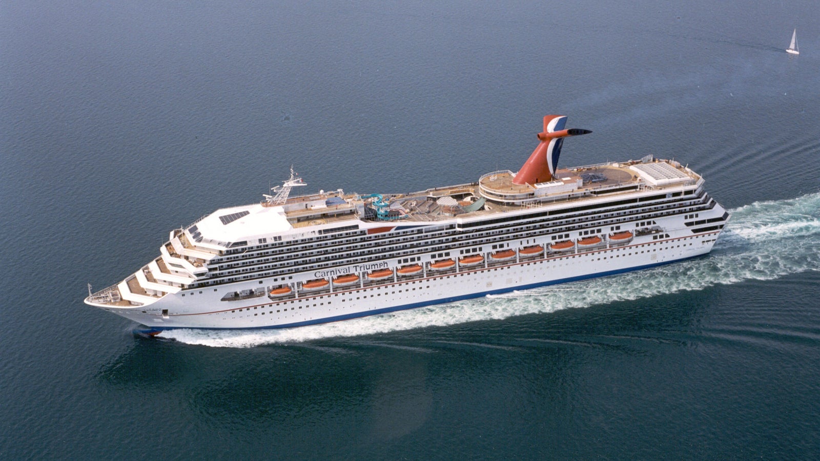Fincantieri | Group - Business - Products - Cruise Ships - Carnival Triumph: Large operational cruise ship sailing on calm open waters, multiple decks including upper recreational areas, distinctive red and blue funnel clearly visible, white exterior and rows of windows.