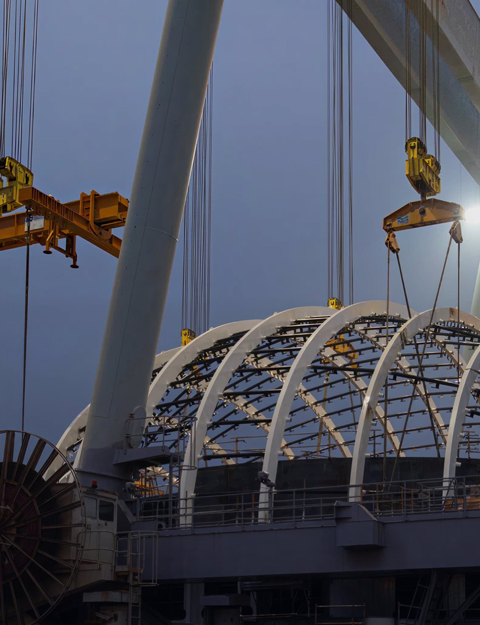 Fincantieri | Gruppo - Sostenibilità - Transizione energetica - Impatti sull'ambiente: Operaio con casco e giacca protettiva all’interno di grande magazzino industriale, soffitti alti, travi metalliche e illuminazione da finestre alte. Ambiente di produzione, enfasi su sicurezza e professionalità.