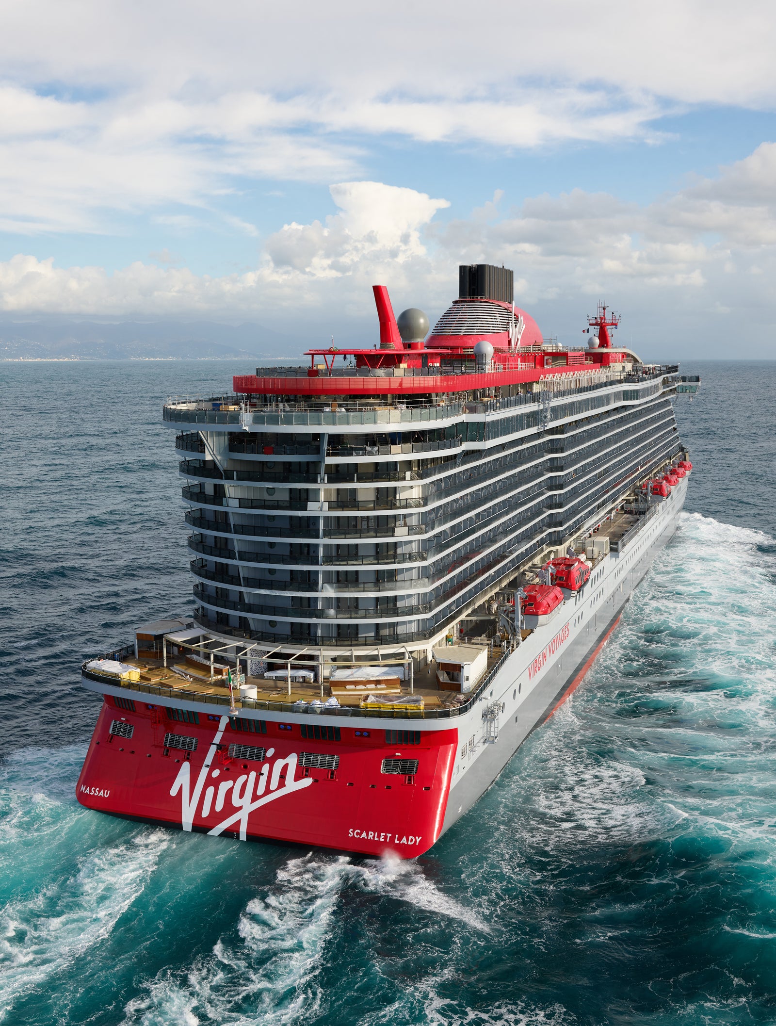 Fincantieri | Group - Business - Products - Cruise Ships - Scarlet Lady: Large operational cruise ship with white and red design, multiple decks with balconies, 'Virgin' logo and 'Scarlet Lady' text prominently visible frontally, sailing on open waters under partly cloudy sky.