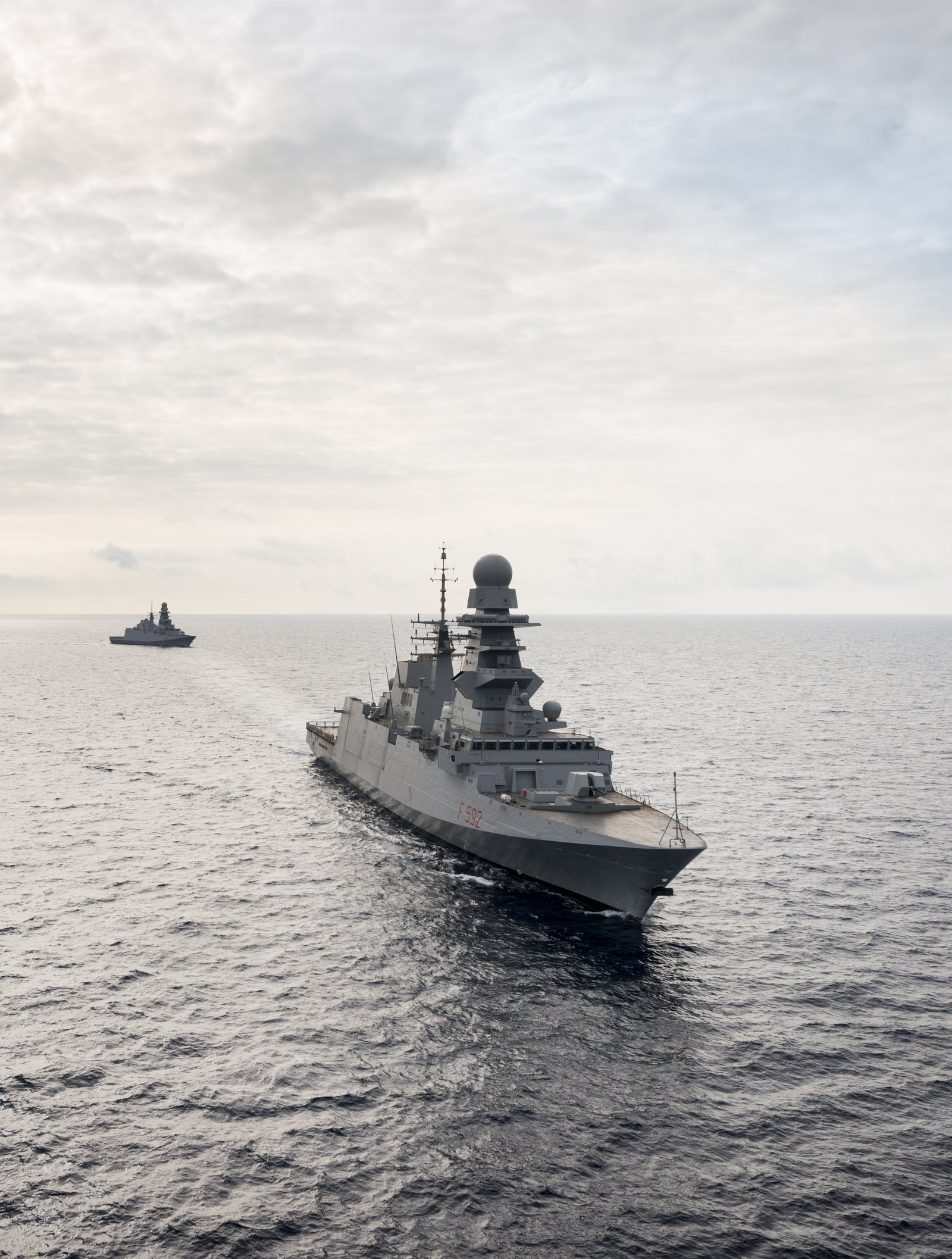  Fincantieri | Gruppo - Business - Prodotti - Navi per la difesa - Fregate - Classe Bergamini: Vista laterale di più navi operative in navigazione, nave principale con radar avanzati e design moderno, atmosfera strategica.