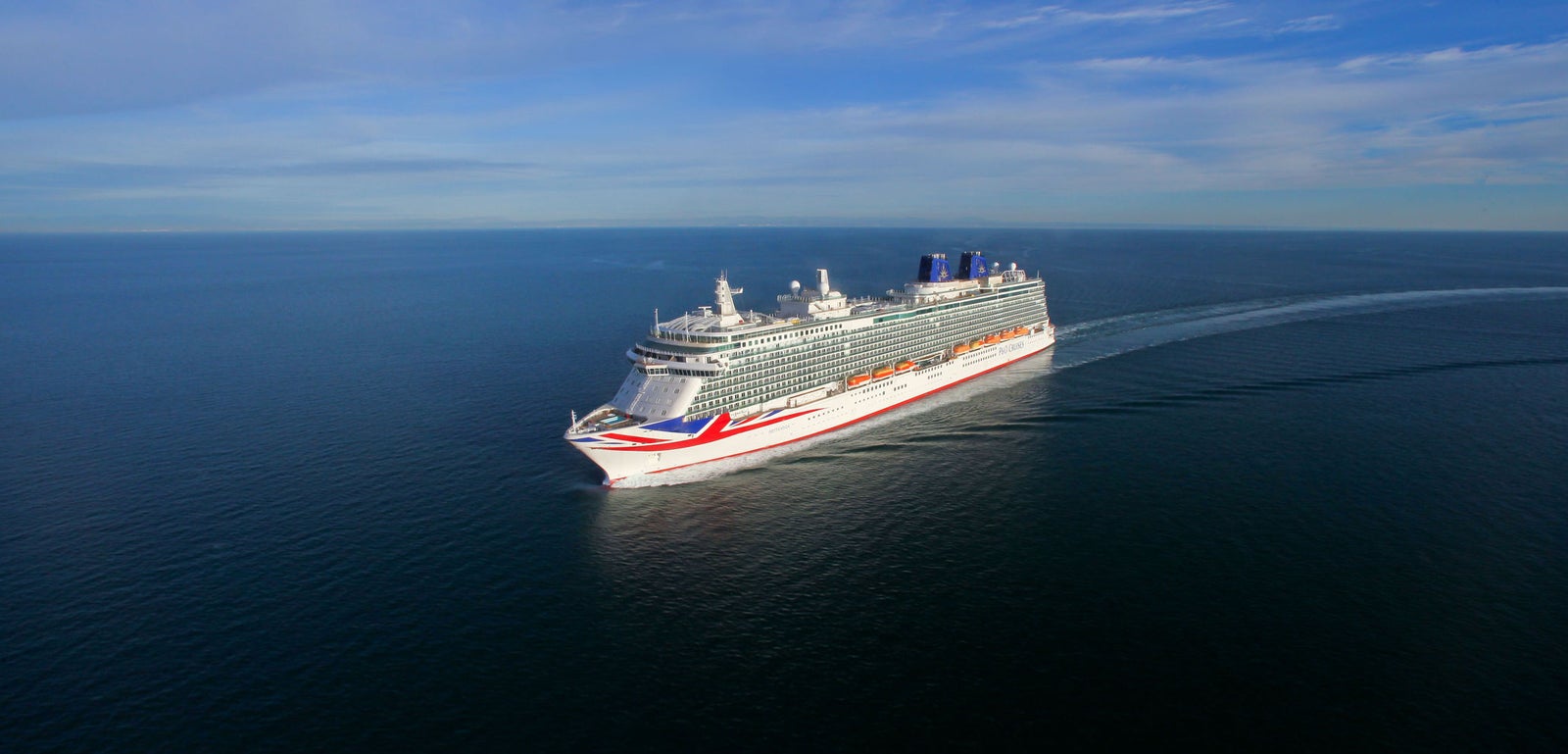 Fincantieri | Group - Business - Products - Cruise Ships - Britannia: Aerial view of Britannia cruise ship in operation navigating open sea, white hull with red and blue accents, multiple passenger decks visible.