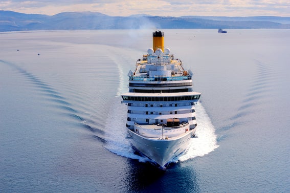 Fincantieri | Gruppo - Business - Prodotti - Navi da Crociera - Costa Luminosa: Grande nave da crociera bianca operativa che naviga su acque calme e aperte sotto cielo parzialmente nuvoloso, scia visibile, colline distanti sull’orizzonte, scena che comunica viaggio e tranquillità.