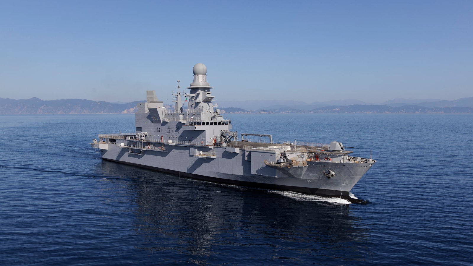  Fincantieri | Gruppo - Business - Prodotti - Navi Militari - Portaerei e Navi Anfibi - AL-FULK: Grande nave militare moderna in operazione, dotata di radar avanzati e design elegante, in navigazione su acque calme e aperte, cielo blu limpido, terra lontana sull’orizzonte.