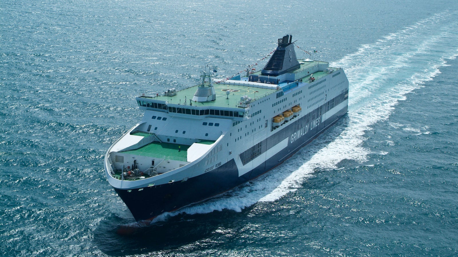 Fincantieri | Group - Business - Products - Ferries - Cruise Roma: Large ferry "GRIMALDI LINES" in operation, green and white color, multiple decks, visible white wake, clear ship name on hull, open sea background.