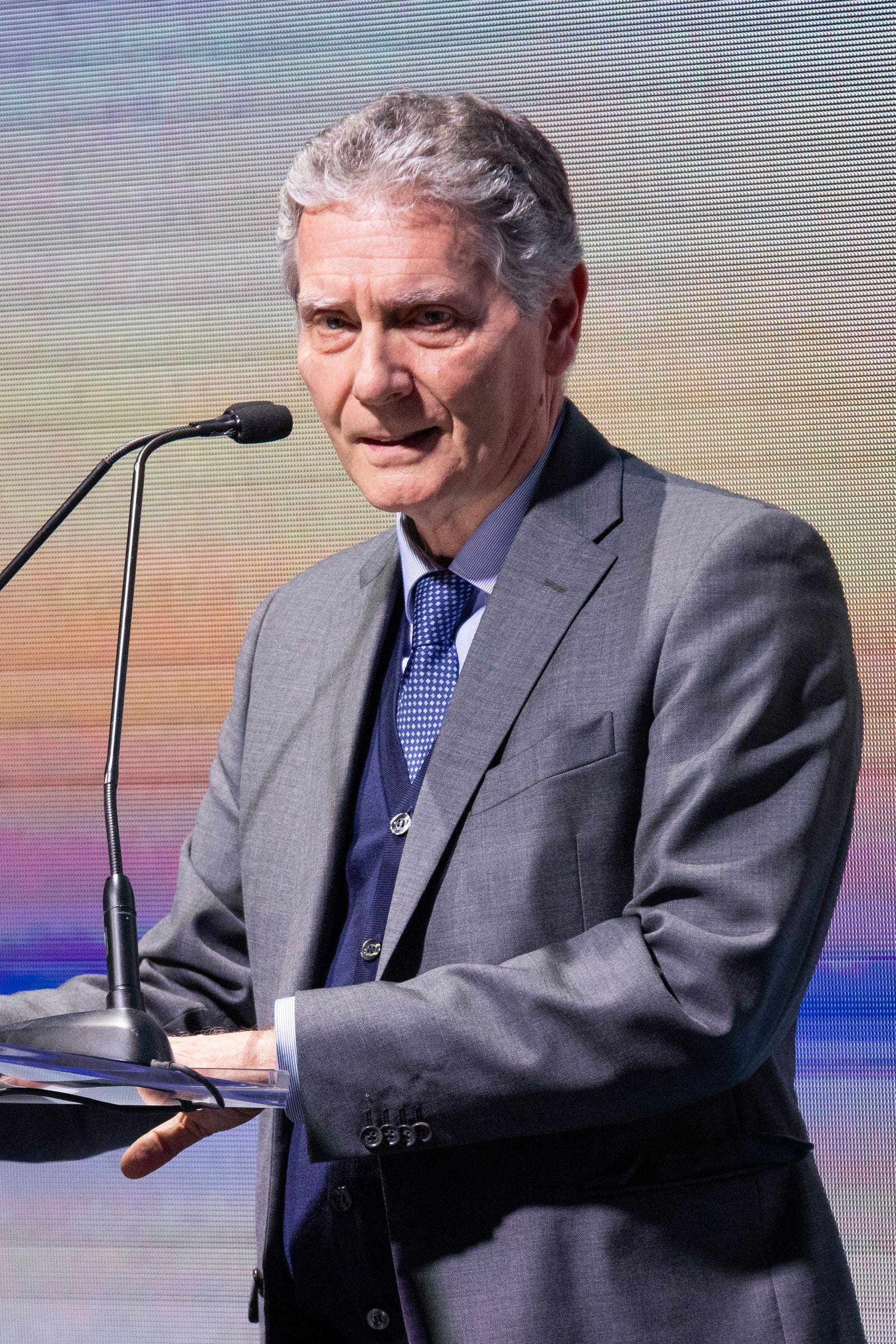 Newsroom - Press releases - 2026 - Fincantieri Group: Fincantieri delivers Norwegian Luna in Marghera: Fincantieri executive in grey suit and blue tie speaks at microphone, colored LED wall in background.