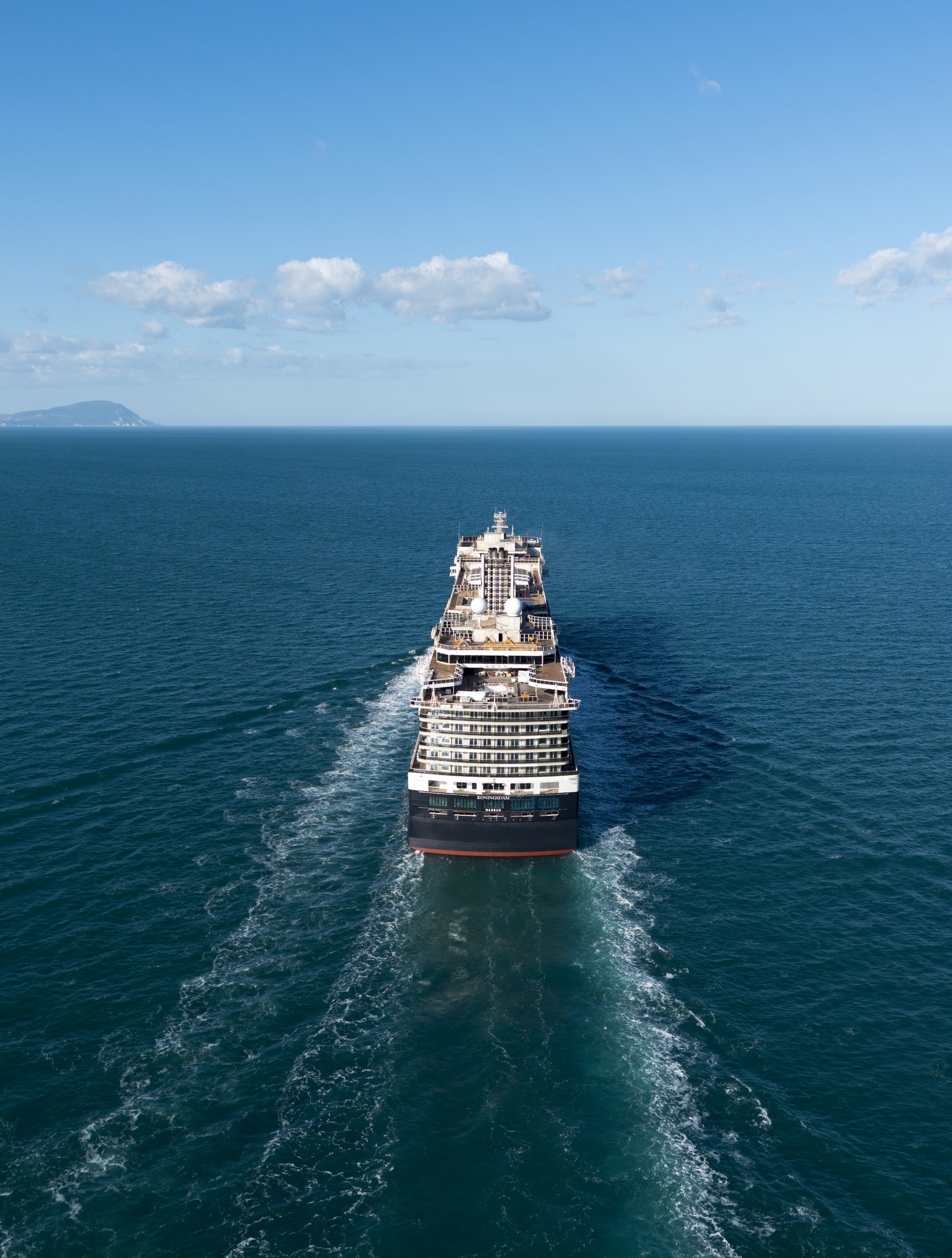 Fincantieri | Gruppo - Business - Prodotti - Navi da Crociera - Koningsdam: Grande nave da crociera operativa che naviga su acque calme e aperte sotto cielo azzurro limpido, scia visibile dietro la nave, ampie vedute dell’oceano.