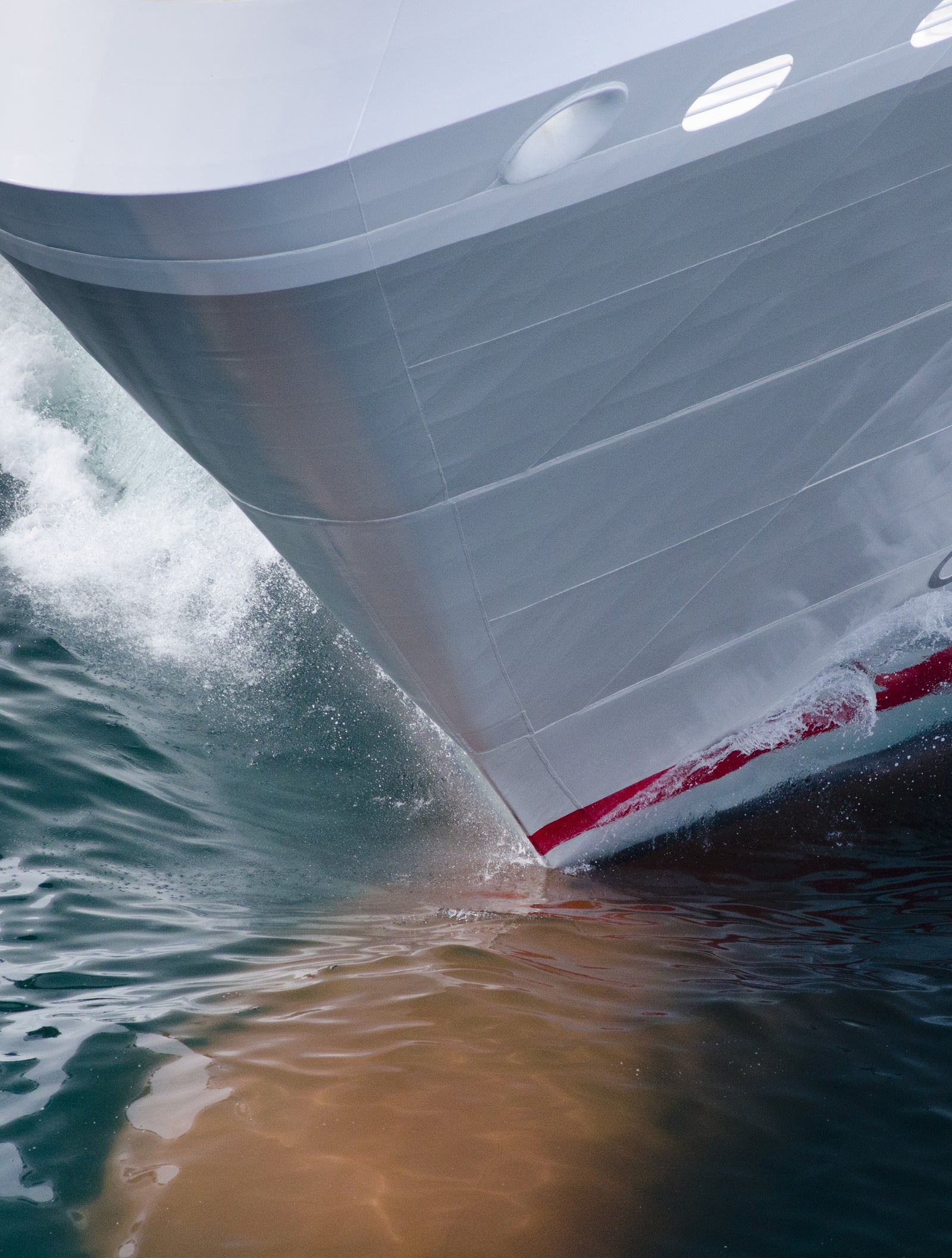 Fincantieri | Group - Business - Products - Cruise Ships - Le Soléal: Sleek ship bow in operation slicing through ocean waves, streamlined design with vibrant red accents, dynamic water motion emphasizes speed and power, setting highlights marine travel and engineering precision.