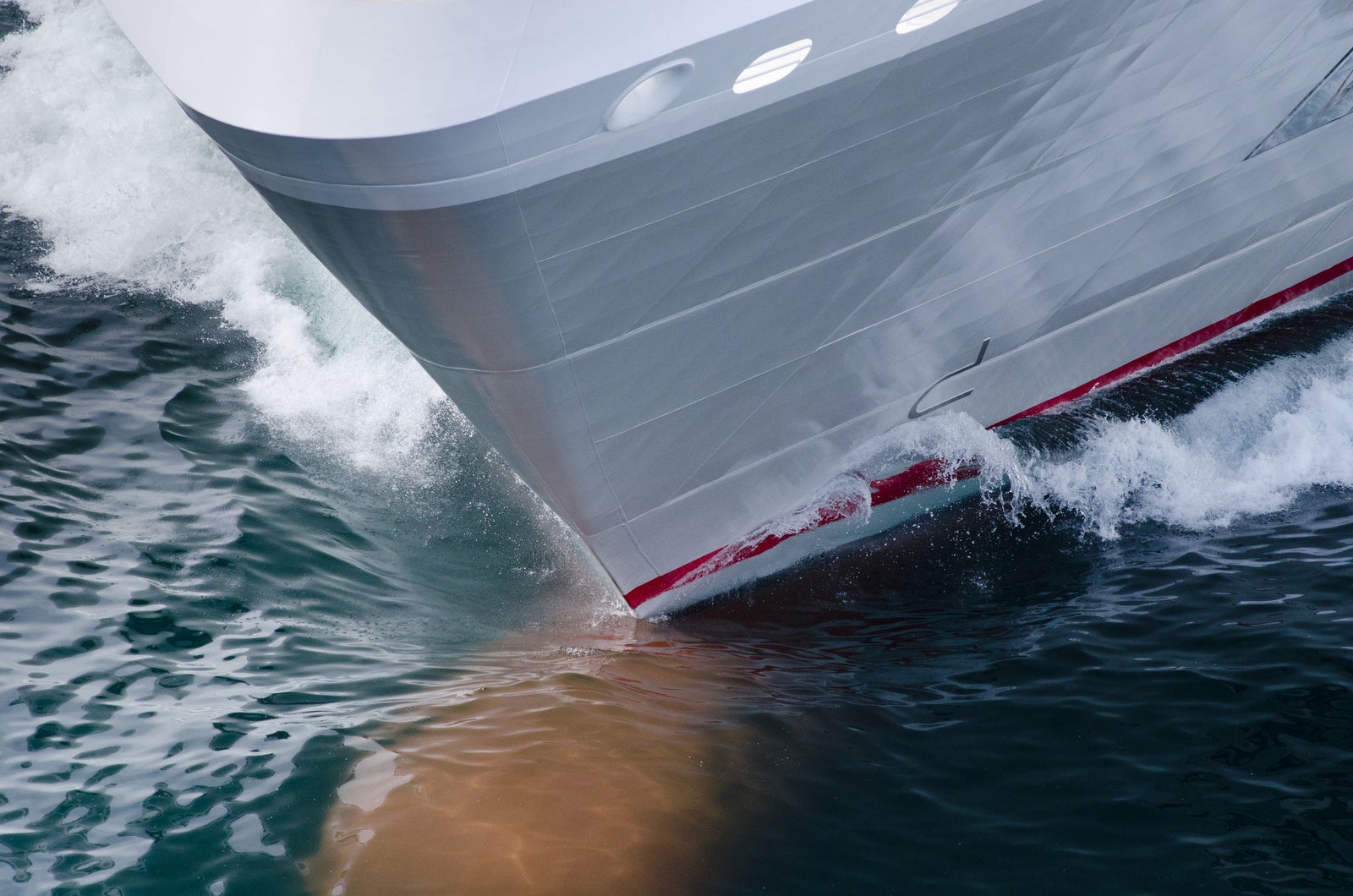 Fincantieri | Group - Business - Products - Cruise Ships - Le Soléal: Sleek ship bow in operation slicing through ocean waves, streamlined design with vibrant red accents, dynamic water motion emphasizes speed and power, setting highlights marine travel and engineering precision.