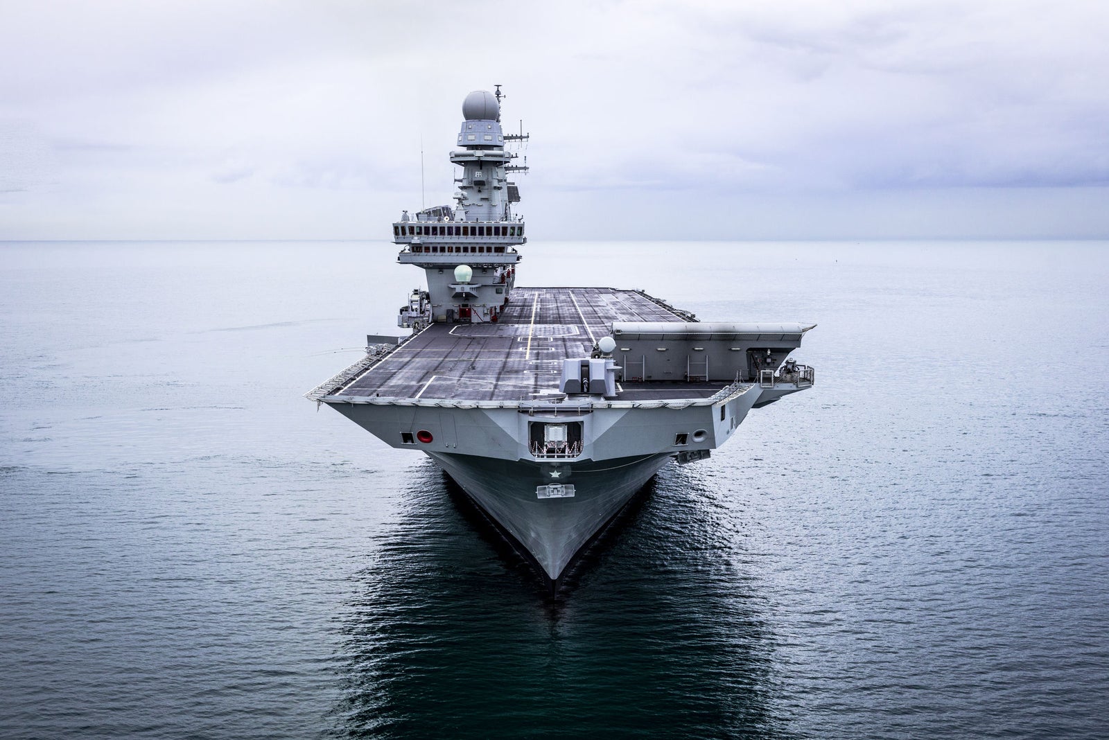 Fincantieri | Group - Business - Products - Naval Vessels - Aircraft Carriers and Amphibious Ships - Cavour: Large aircraft carrier viewed from the front, imposing structure, sitting on calm, overcast sea.