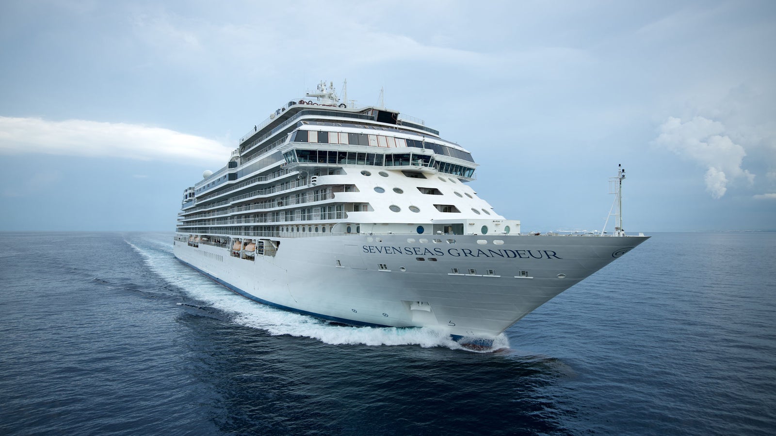 Fincantieri | Group - Business - Products - Cruise Ships - Seven Seas Grandeur: Large white cruise ship in operation, front view, visible wake, calm sea and slightly cloudy sky on horizon.