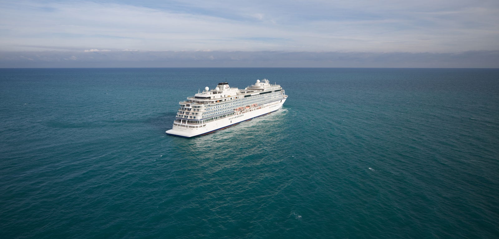Fincantieri | Group - Business - Products - Cruise Ships - Viking Saturn: Spacious white cruise ship in operation, navigating calm open waters under partly cloudy sky, multiple decks, setting provides luxurious travel experience, tranquil ocean and expansive horizon.