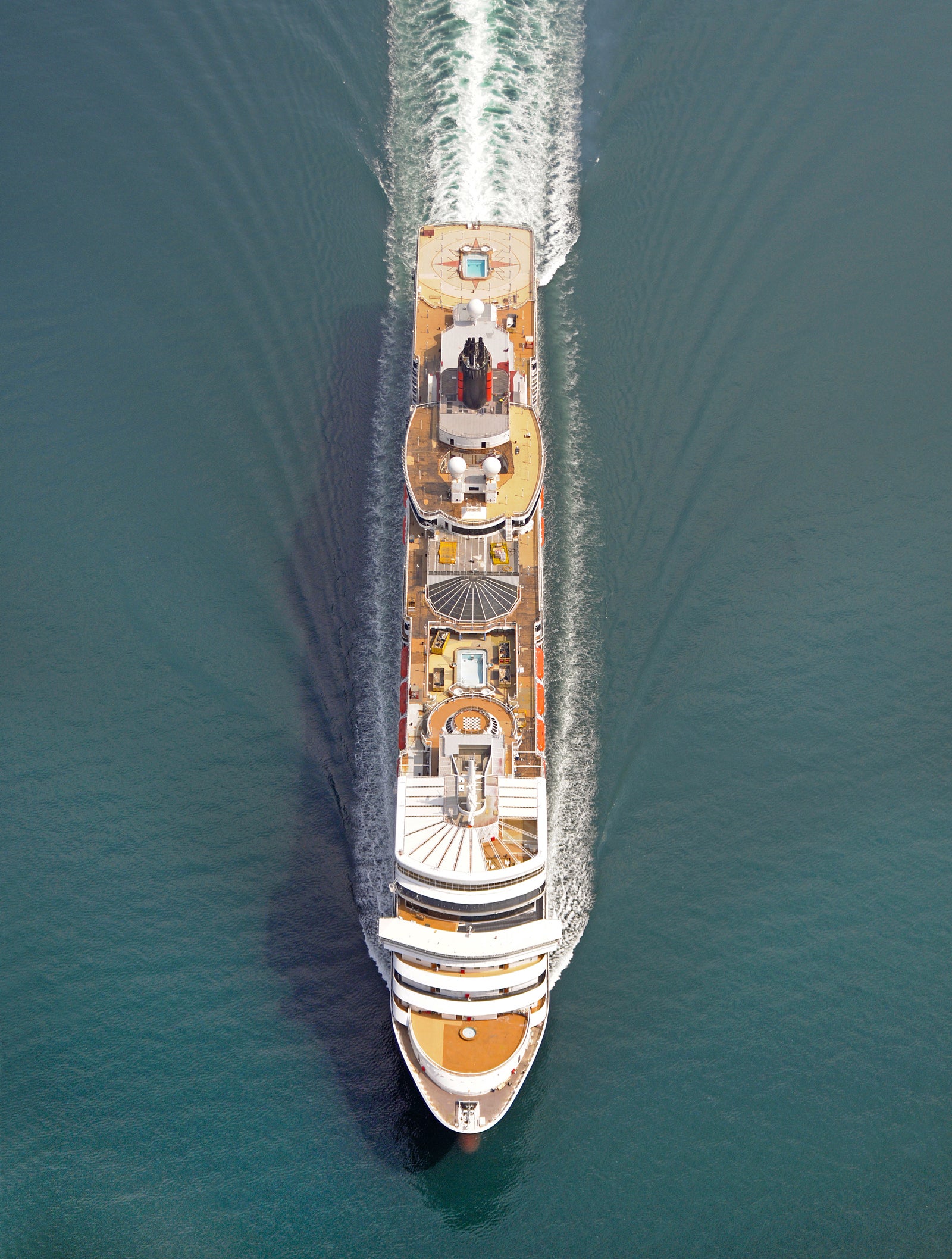 Fincantieri | Group - Business - Products - Cruise Ships - Queen Elizabeth: Aerial view of Queen Elizabeth cruise ship in operation navigating open sea with well-defined symmetrical wake, multiple passenger decks with visible pools and outdoor areas.