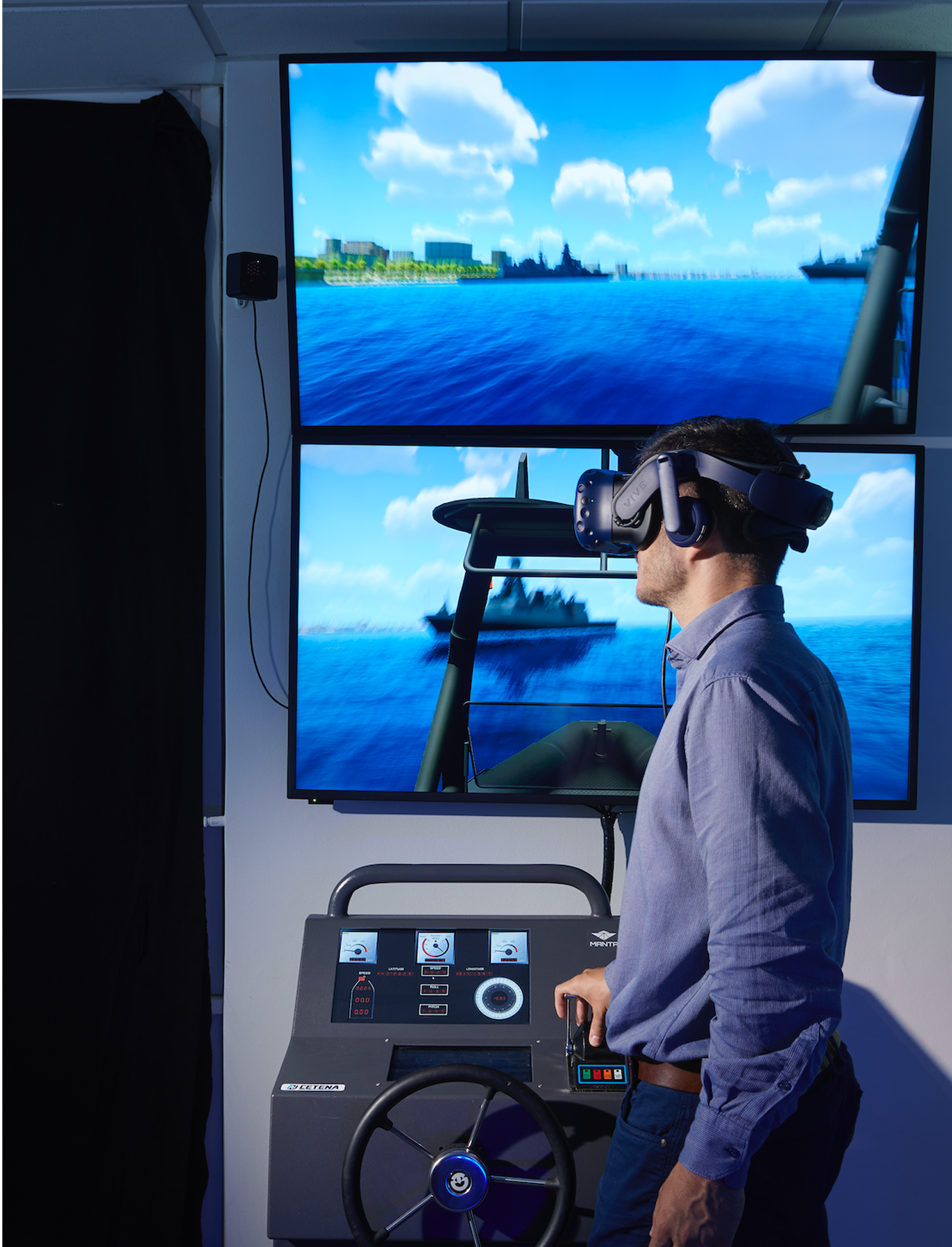 Fincantieri | Group - Subsidiaries and Affiliates - Fincantieri NextTech: Man interacts with virtual reality simulation setup featuring steering console and dual screens displaying naval scene with ships and coastal environment under bright blue sky; VR headset and simulation equipment suggest immersive experience in a controlled indoor environment.