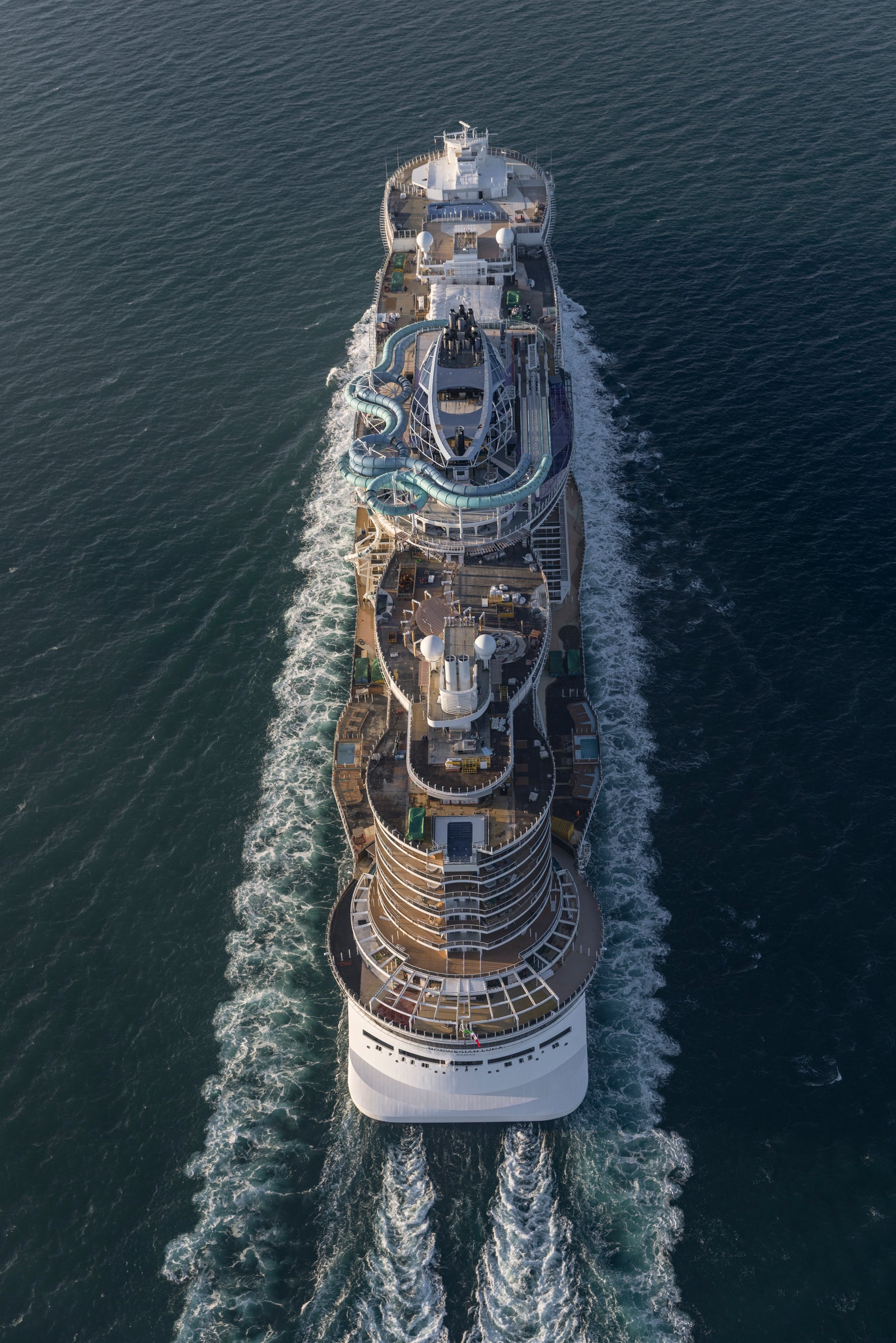  Fincantieri | Group - Business - Products - Cruise Ships - Norwegian Luna: Aerial side view of Norwegian Aqua cruise ship in operation, sailing on calm sea, visible white wake trail.