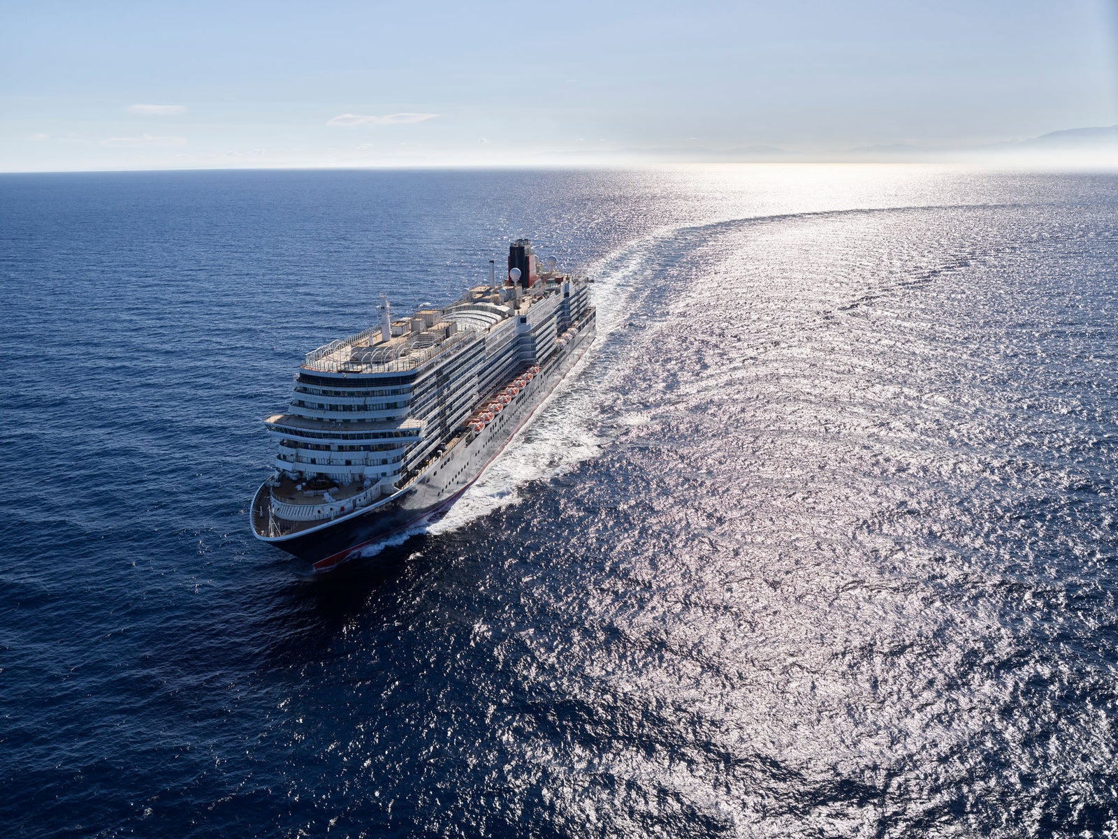 Fincantieri | Group - Business - Products - Cruise Ships - Queen Anne: Side view of cruise ship in operation, navigating open sea, visible white wake in water, linear profile hull, multiple passenger decks.