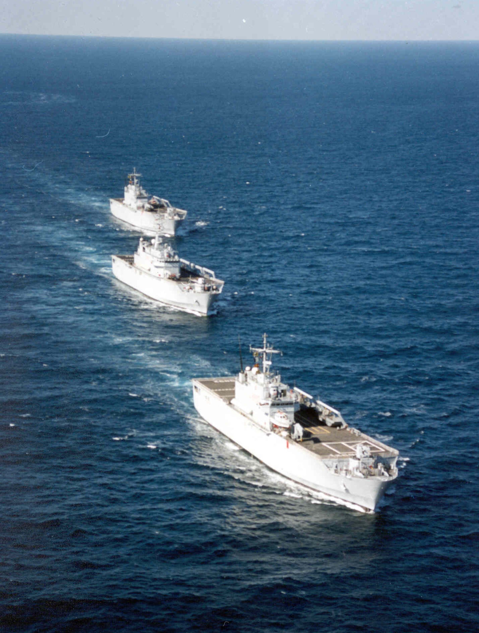 Fincantieri | Gruppo - Business - Prodotti - Navi Militari - Portaerei e Navi Anfibi - Classe San Giusto: Tre navi militari bianche in formazione, ponti ampi, in navigazione su oceano calmo, acqua e cielo blu, destinate a scopi militari o di trasporto.