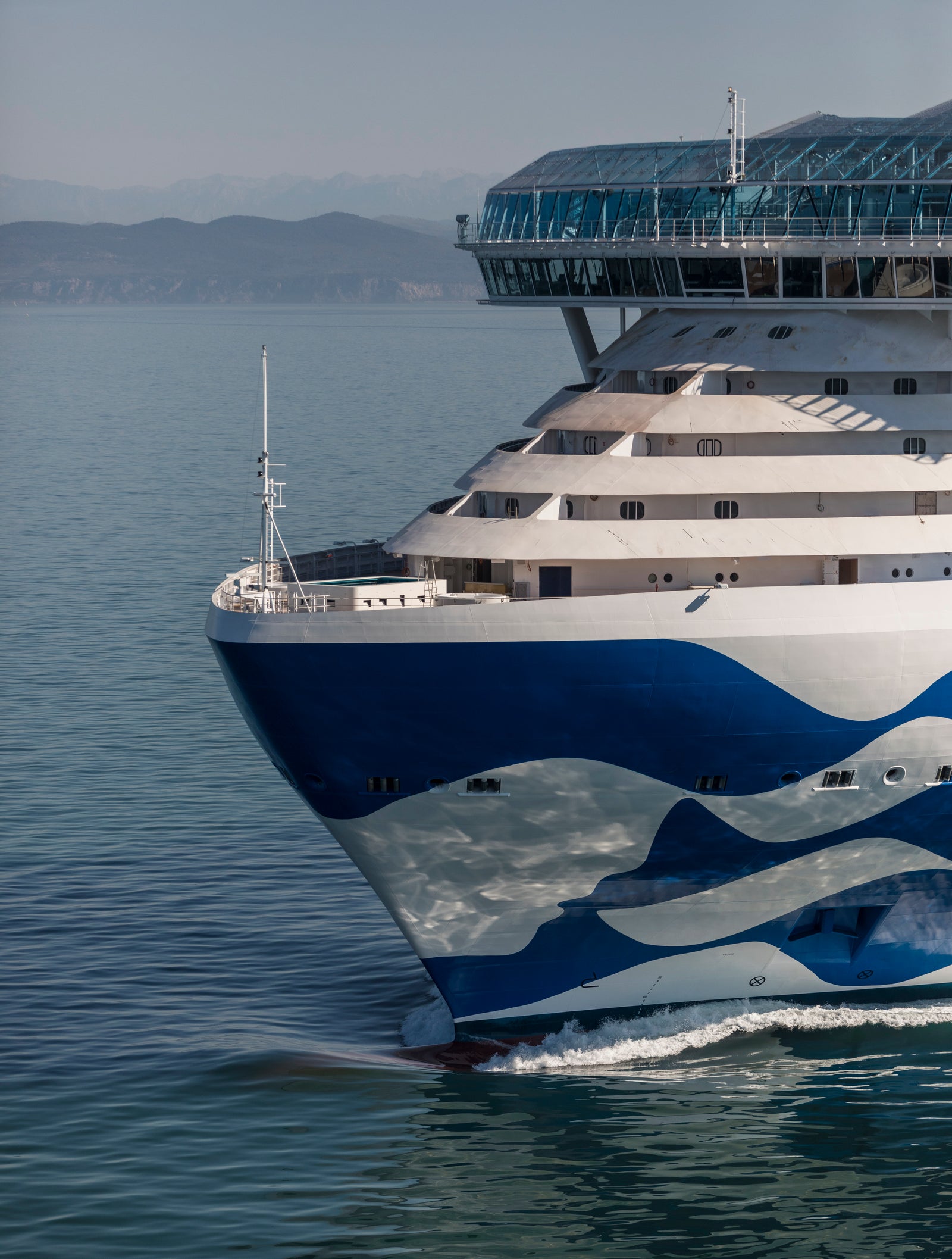  Fincantieri | Gruppo - Business - Prodotti - Navi da Crociera - Star Princess: Large luxury cruise ship with blue and white wave design gliding through calm waters, multiple decks, glass-covered upper section, distant mountains and clear sky.