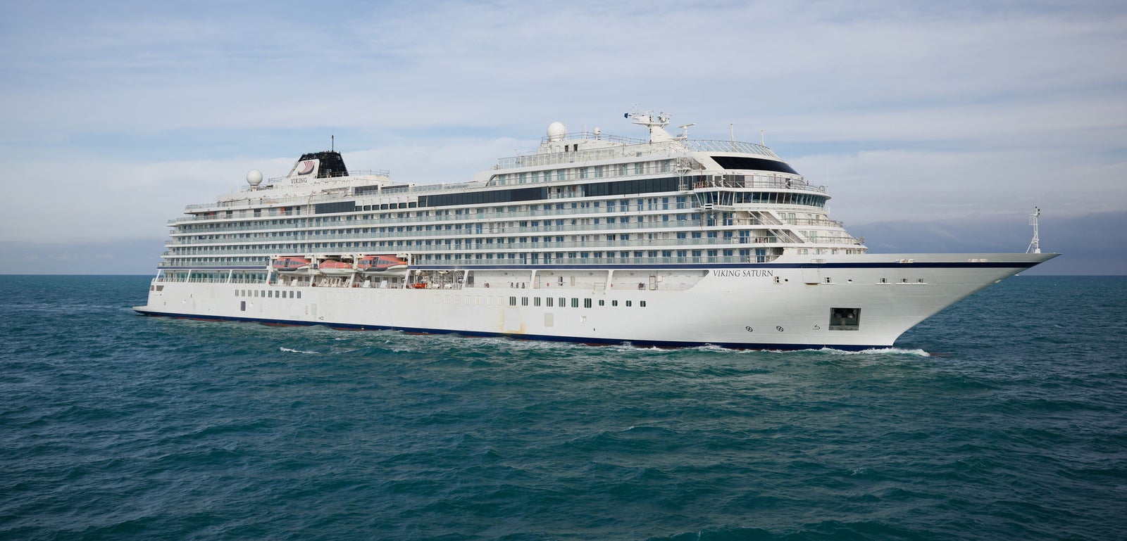 Fincantieri | Group - Business - Products - Cruise Ships - Viking Saturn: Large modern cruise ship in operation, gliding through calm ocean waters under partly cloudy sky, multiple decks and expansive windows, setting highlights grandeur, leisure and travel.