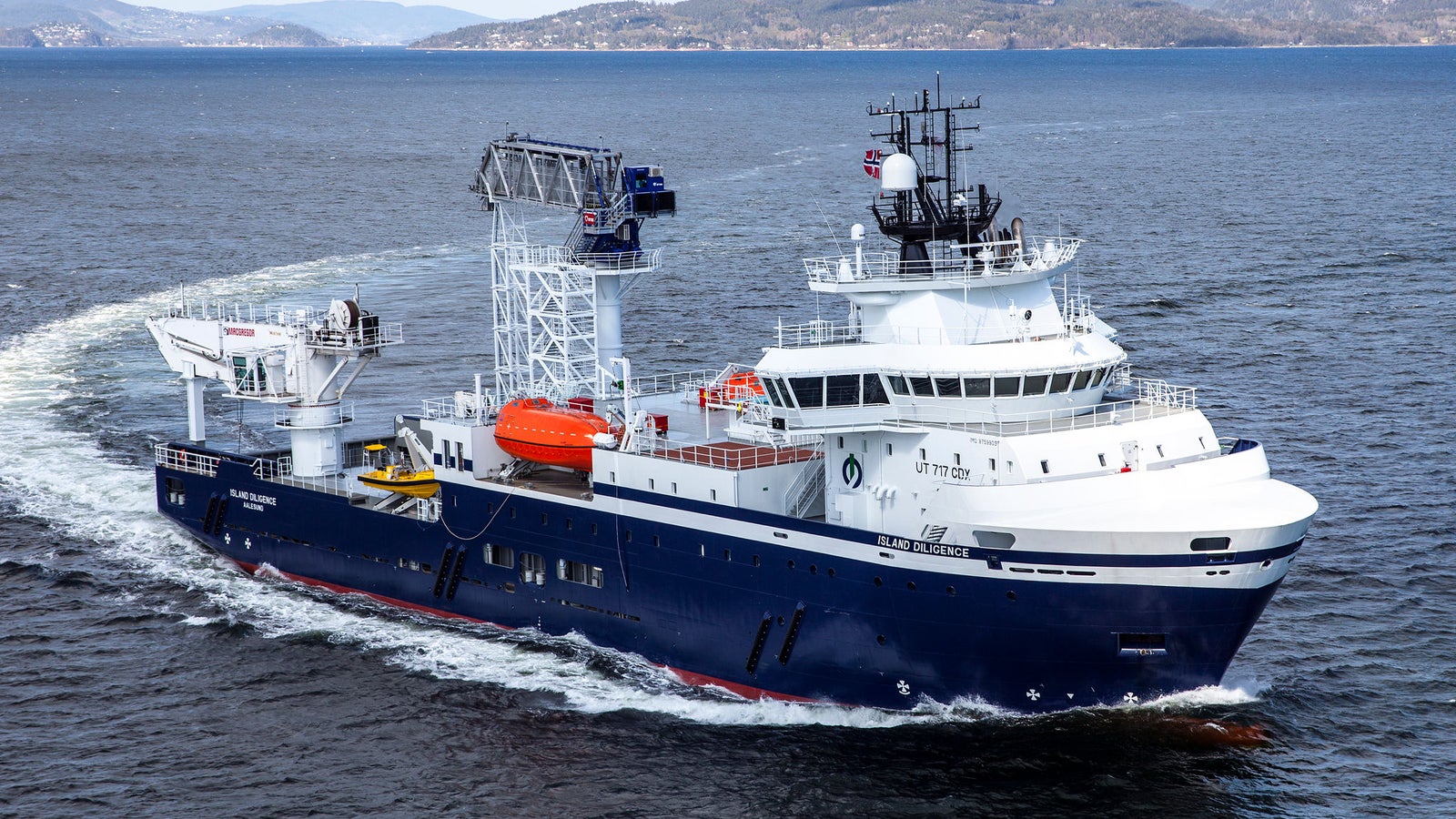 Prodotto - Offshore Support Vessel Island Diligence: Vista laterale della nave operativa in navigazione, scafo blu profondo, sovrastruttura bianca, gru e scialuppe visibili, numero 37 ben evidente sullo scafo, sfondo collinare.