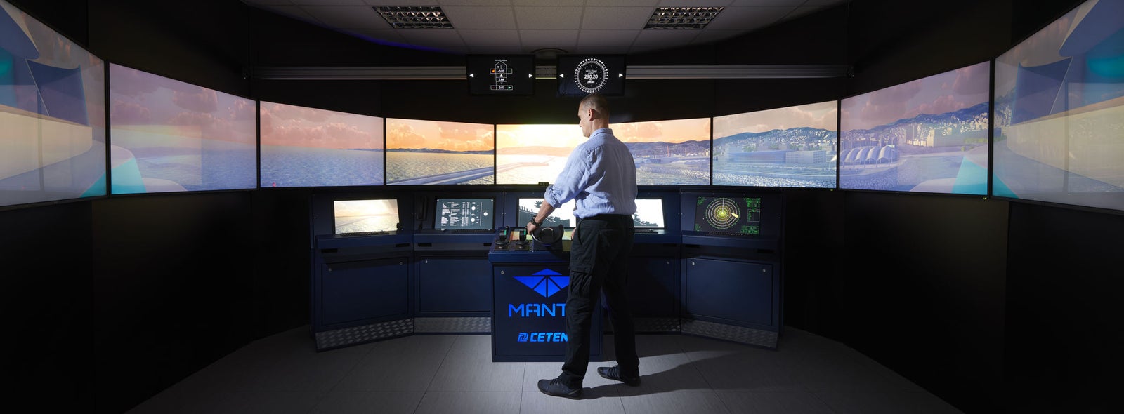 Fincantieri | Group - Business - Products - Cybersecurity - Simulation system (MANTIS): Man stands at center of high-tech maritime simulation system, surrounded by multiple large screens displaying nautical visuals; professional training or control room with dim lighting, 'MANTIS' and logo clearly visible on central console.