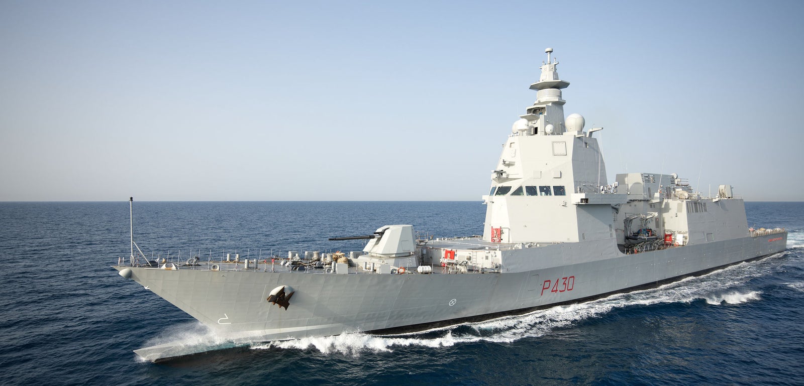 Fincantieri | Gruppo - Business - Prodotti - Navi per la difesa - Fregate - Classe Thaon de Revel: Nave militare moderna grigia in operazione, sovrastruttura alta, in navigazione su acque blu calme, cielo limpido, scia visibile dietro la nave.